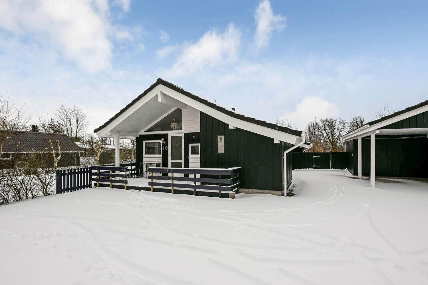 Schwarzes Holzhaus mit weißem Dach und Schneebedecktem Grundstück.