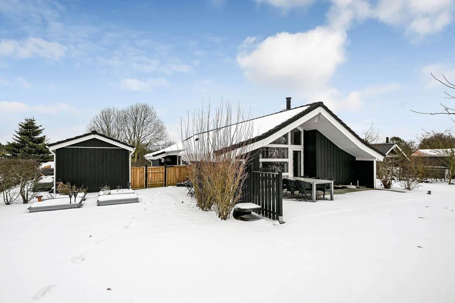 Schwarz-weißes Haus mit Schneebedecktem Garten und Terrasse.