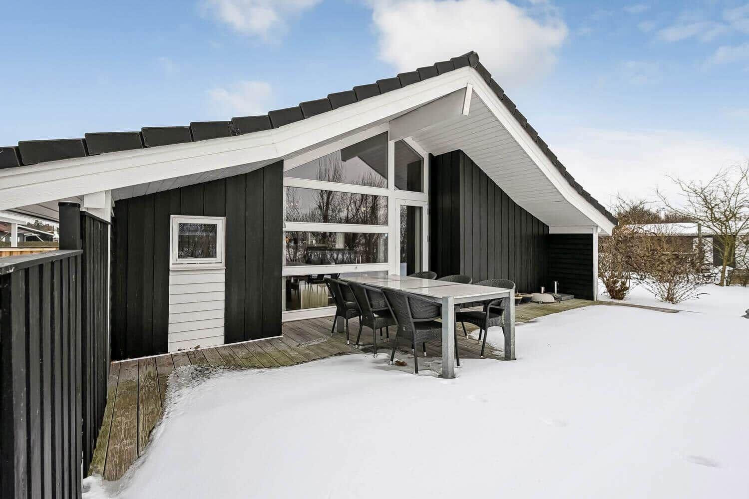 Moderne Holzhütte mit großem Terrassenbereich und Sitzgelegenheiten im Schnee.