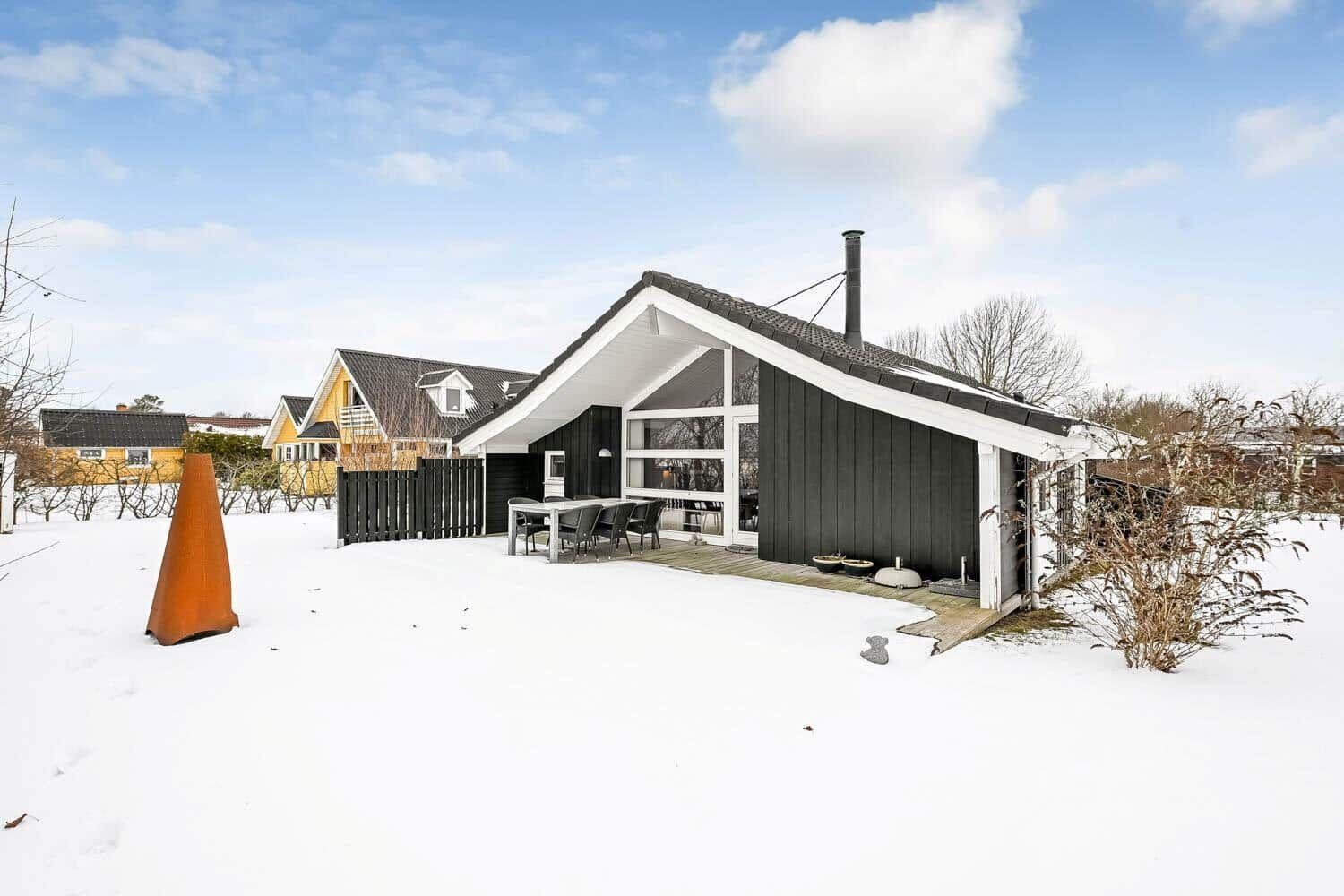Schwarzes Haus mit weißem Dach und Terrasse im Schnee.
