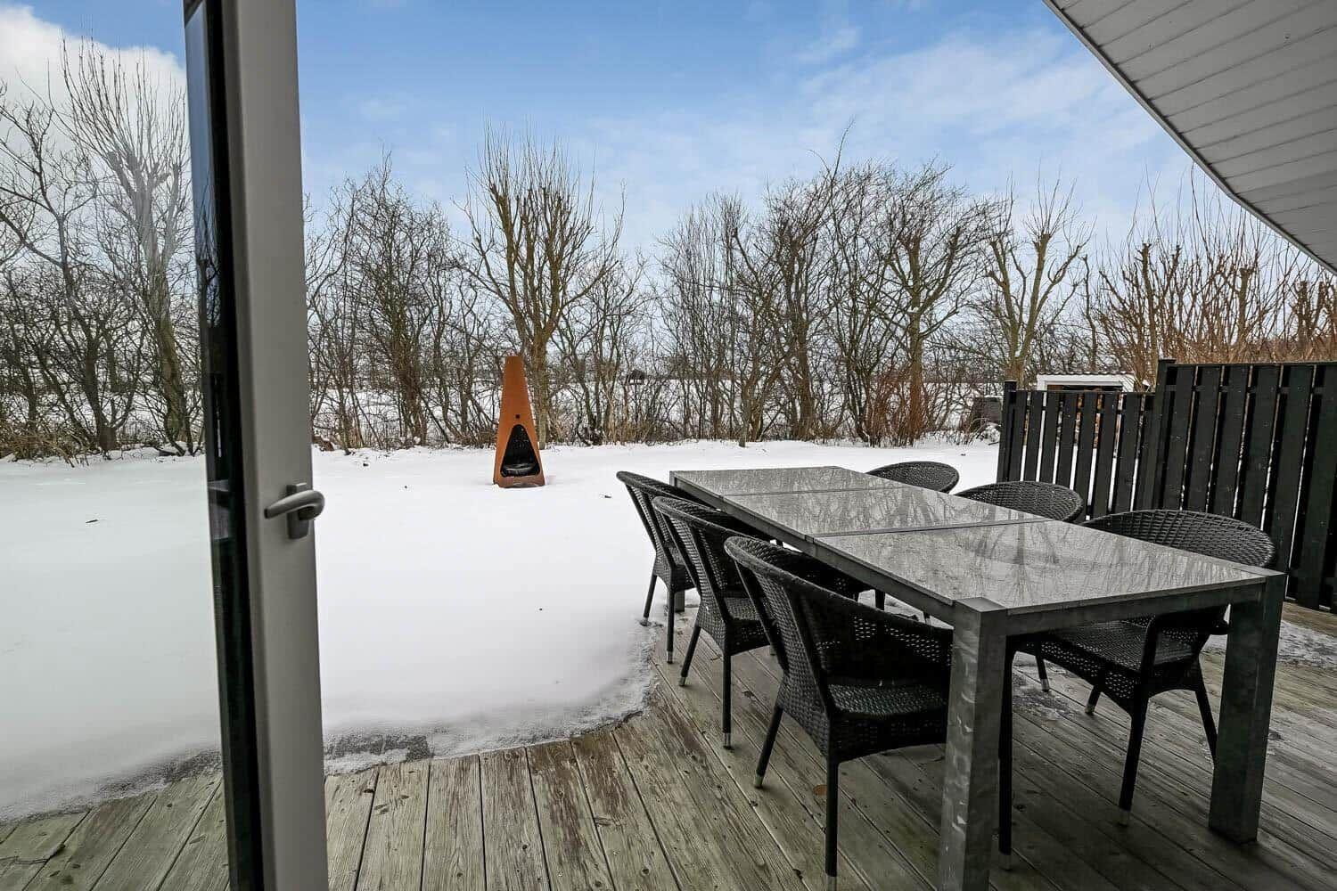 Terrasse mit Tisch und Stühlen, Schnee im Hintergrund, Holzdecke und Feuerstelle.