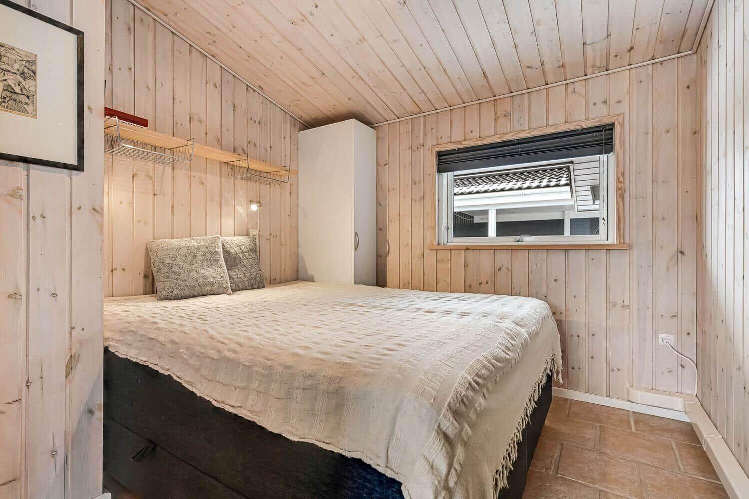 Schlafzimmer mit Holzwand, Bett, Kleiderschrank und Fenster.