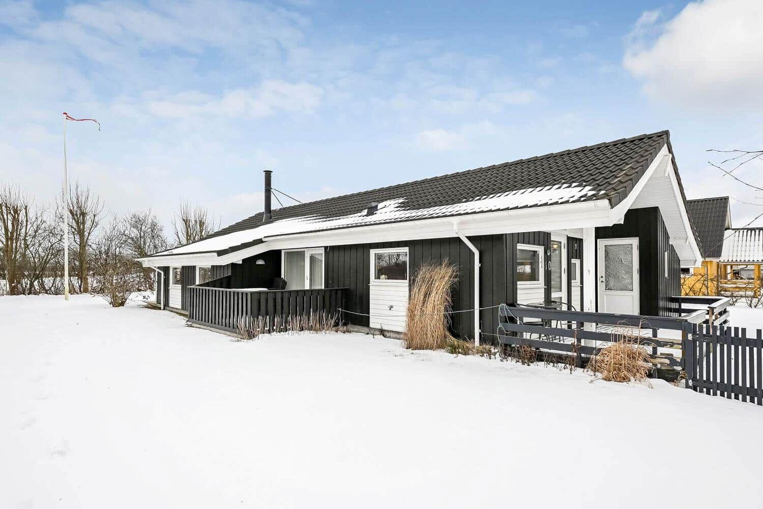 Schwarzes Holzhaus mit weißem Dach und Terrasse im Schnee.