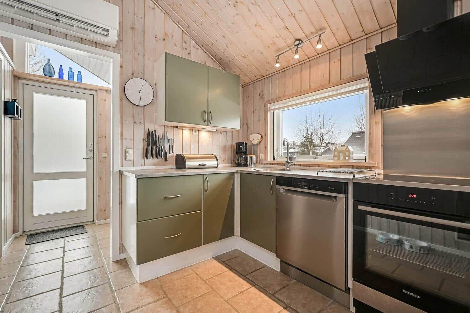Küche mit Holzwand, grünen Schränken und moderner Geräteausstattung.