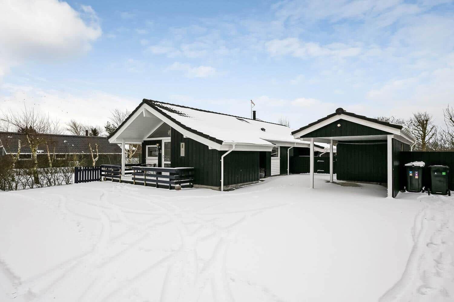 Schwarzes Holzhaus mit Schneebedecktem Dach und Garage im Winter.