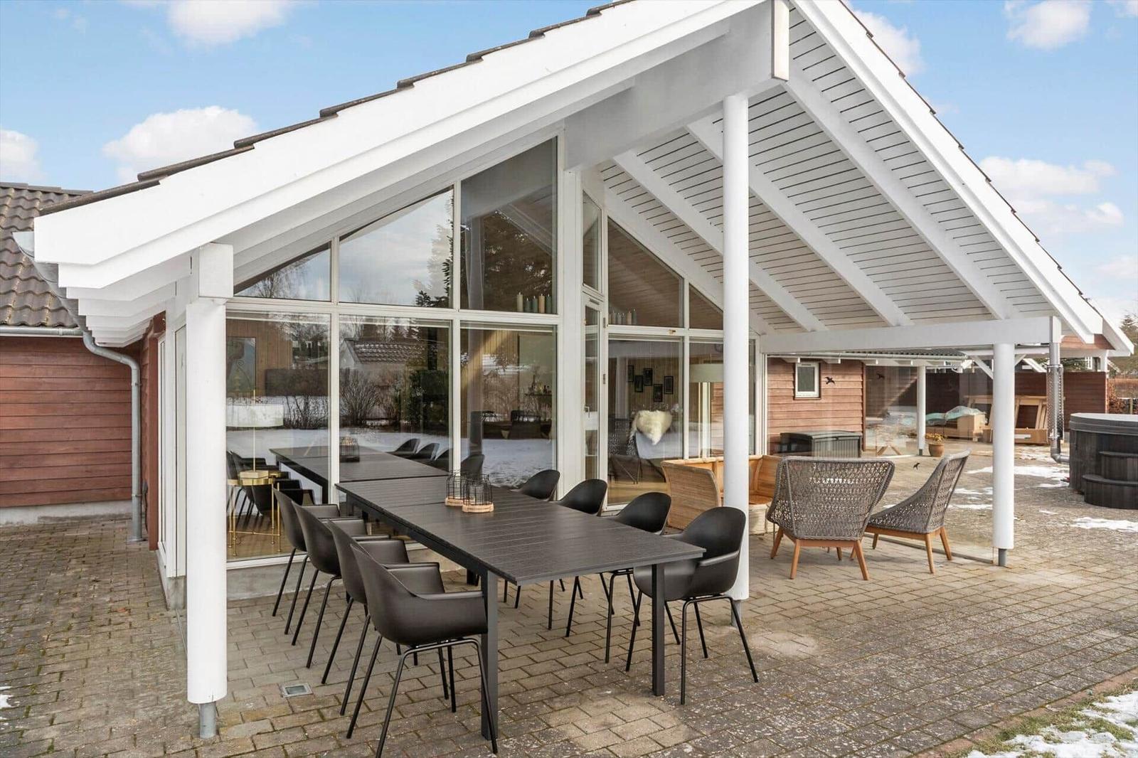Patio with table and chairs under white roof. Large windows show living area.