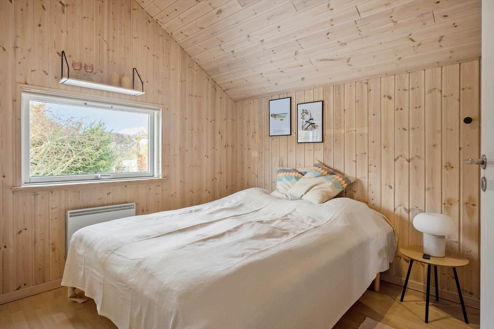 Bedroom with wooden walls, bed, window, and nightstand.
