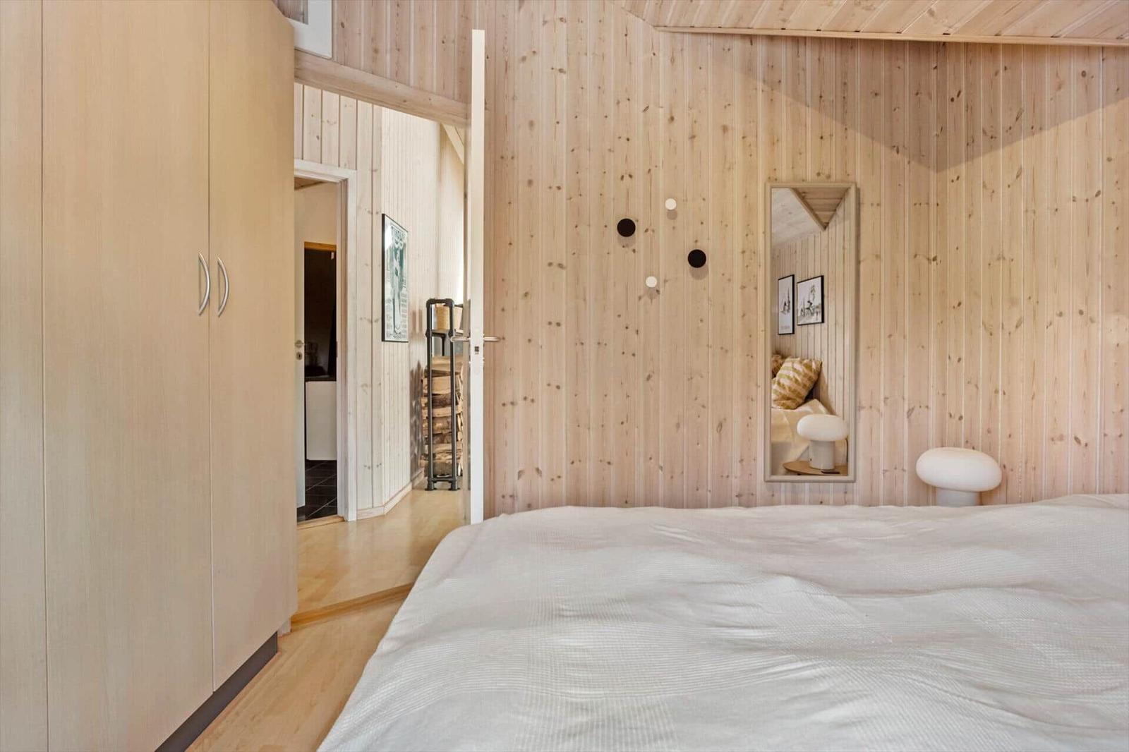 Bedroom with wooden wall, bed, mirror, and wardrobe.