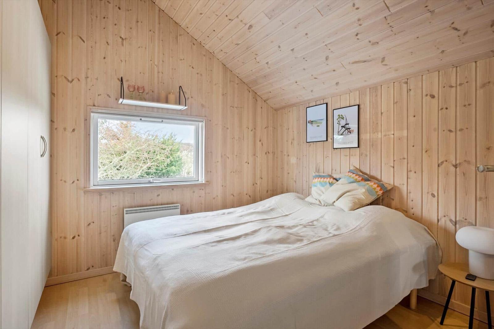 Bedroom with wooden walls, bed, and window.