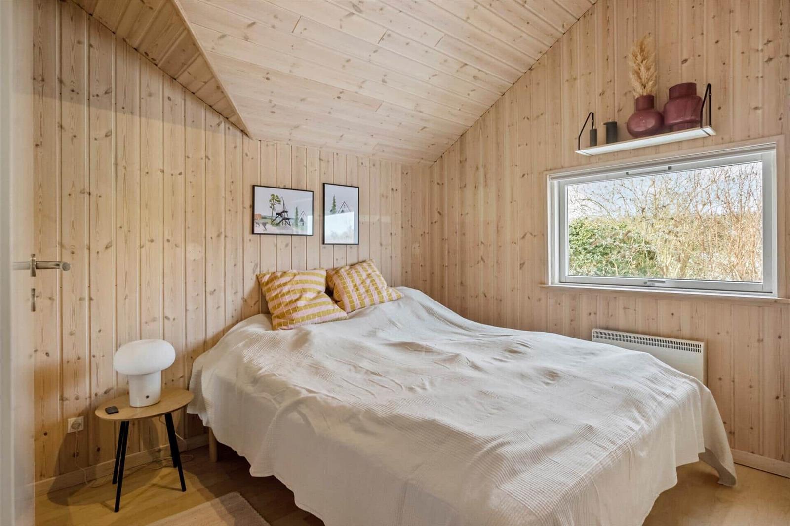 Bedroom with wooden walls, bed, window, and nightstand.