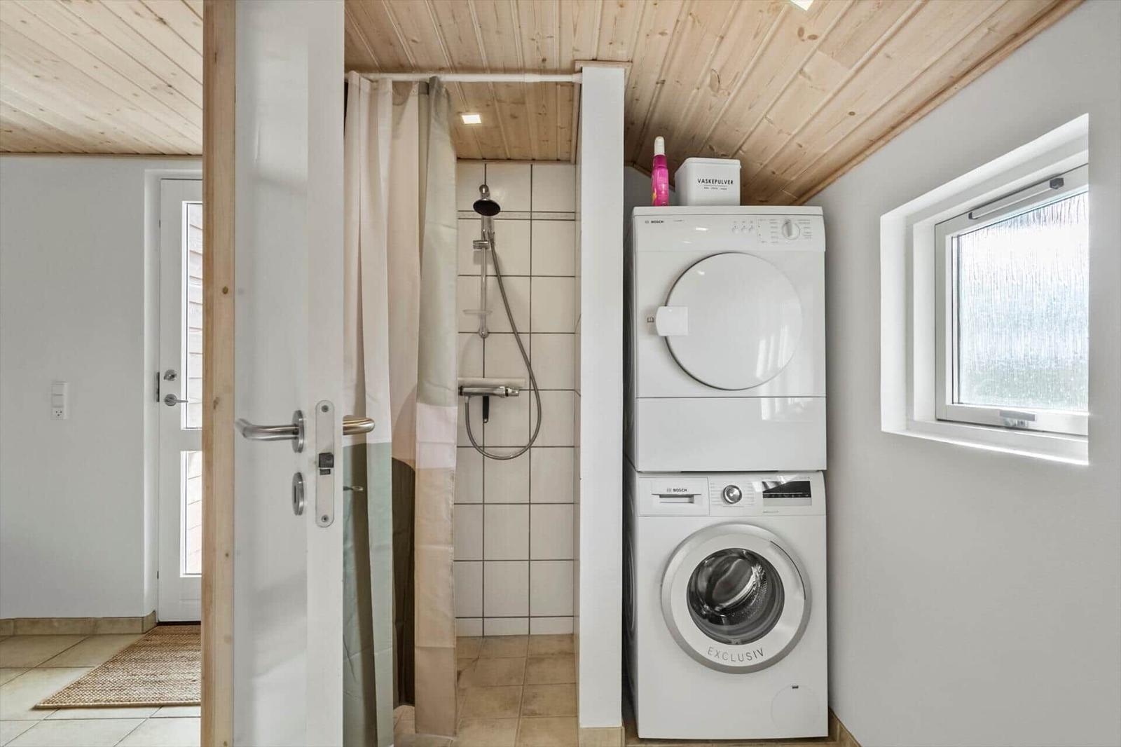 Shower with curtain and stacked washer-dryer unit.