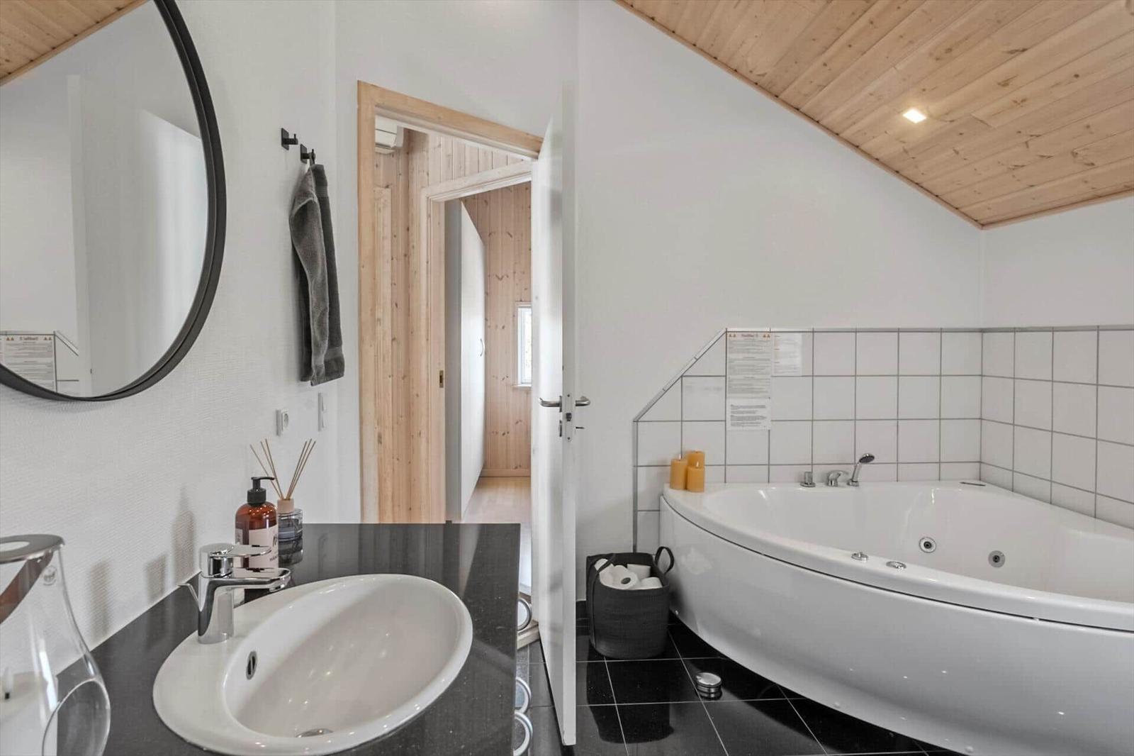 Bathroom with bathtub, sink, and mirror. Wooden ceiling and white walls.