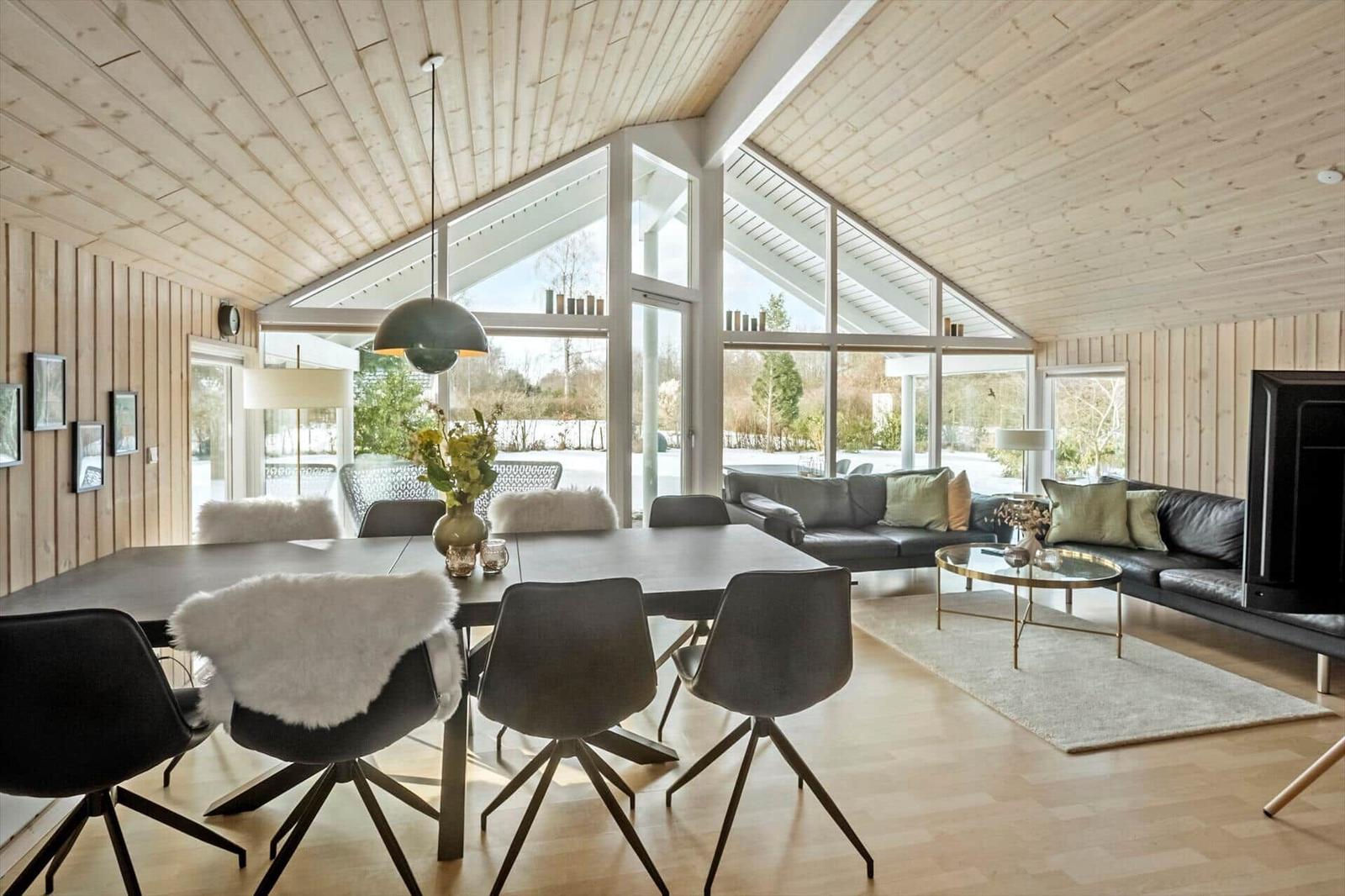 Large living and dining area with wooden ceiling, large windows, and modern furnishings.
