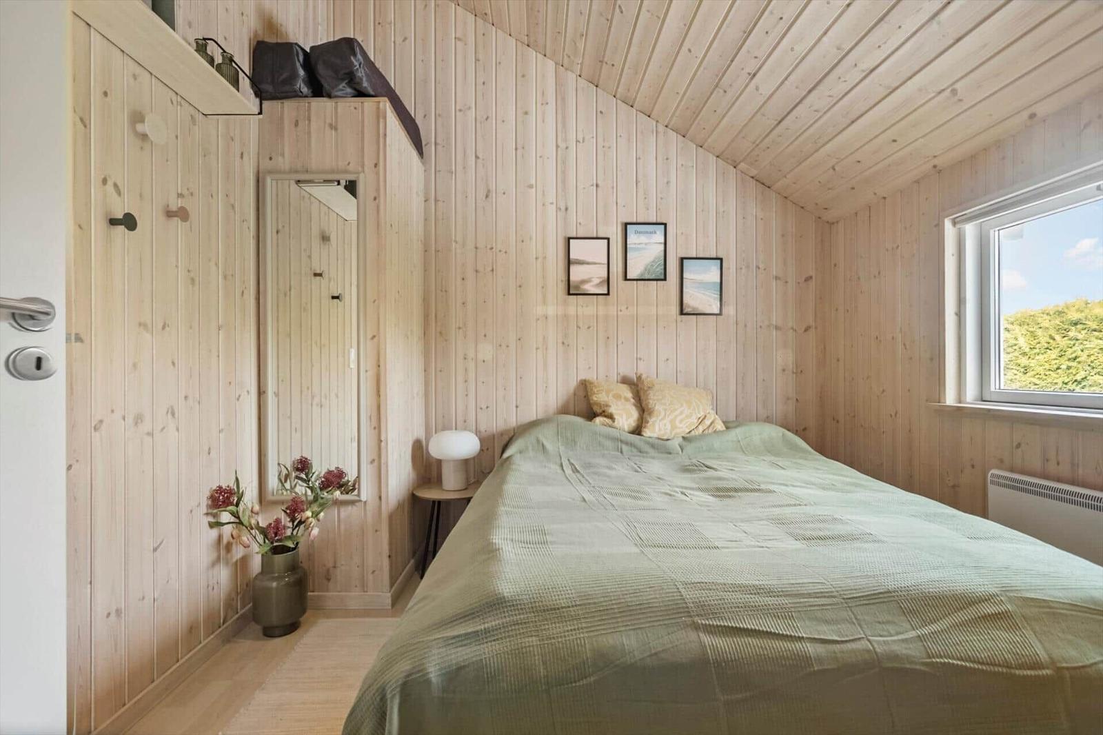 Bedroom with wooden walls, bed, window, and mirror.