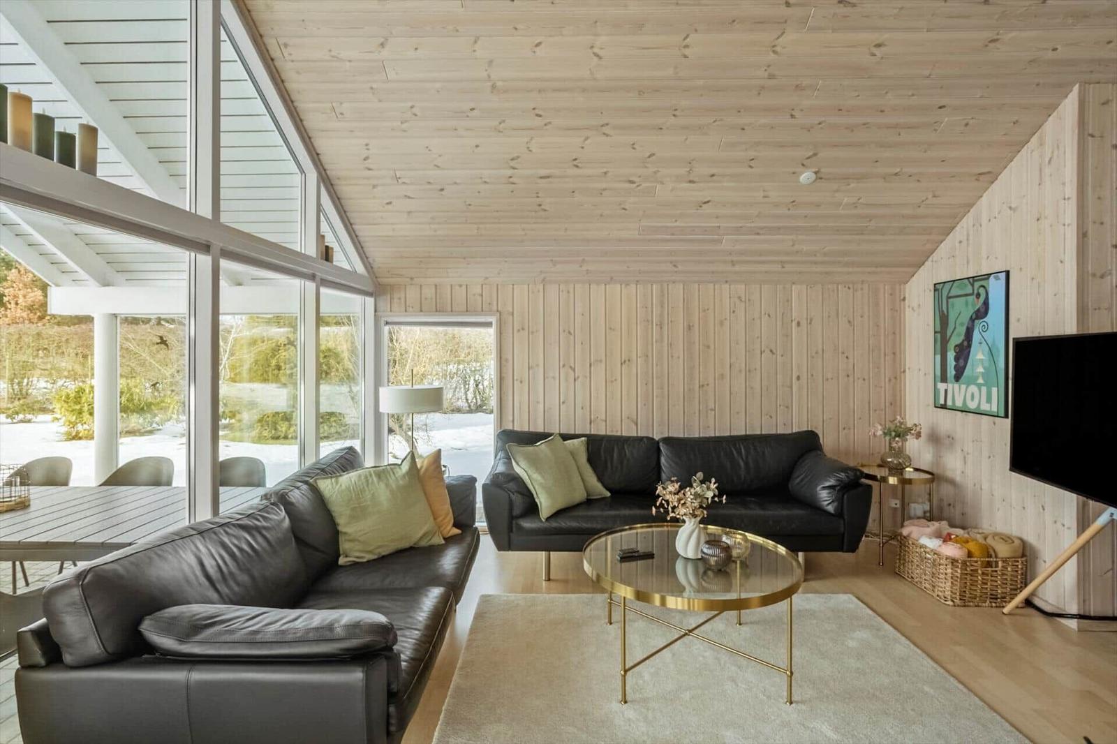 Living room with two black sofas, glass table, and wooden wall.