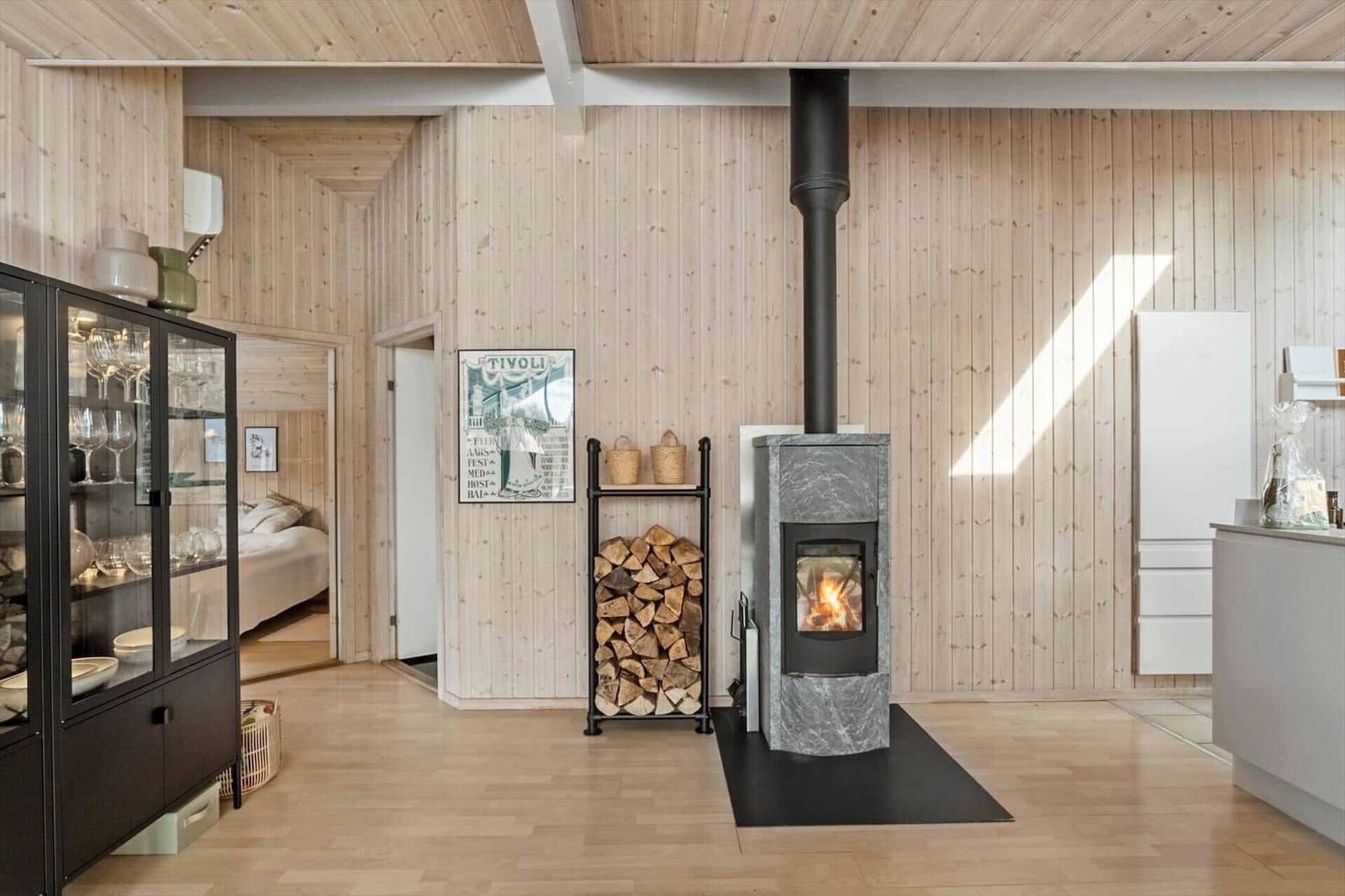 Living room with wood stove, firewood stack, and glass cabinet. Bedroom in background.