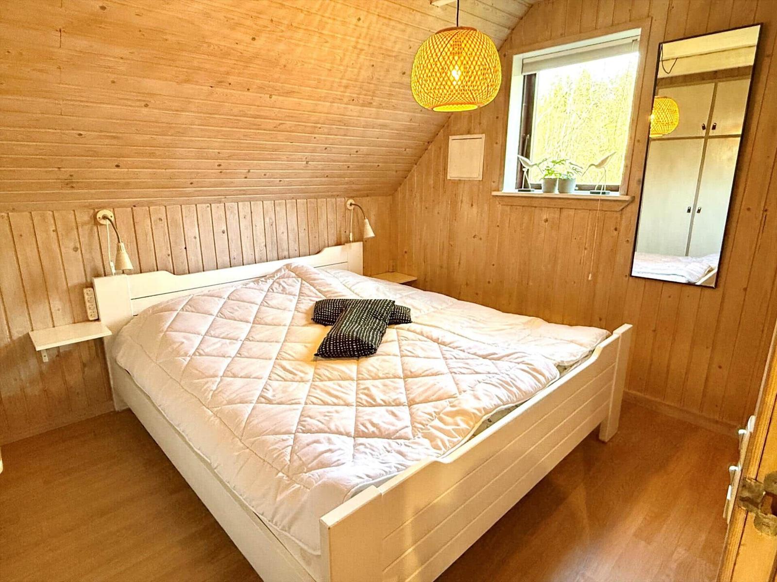Schlafzimmer mit Holzwand, weißem Bett und Fenster mit Pflanzen.