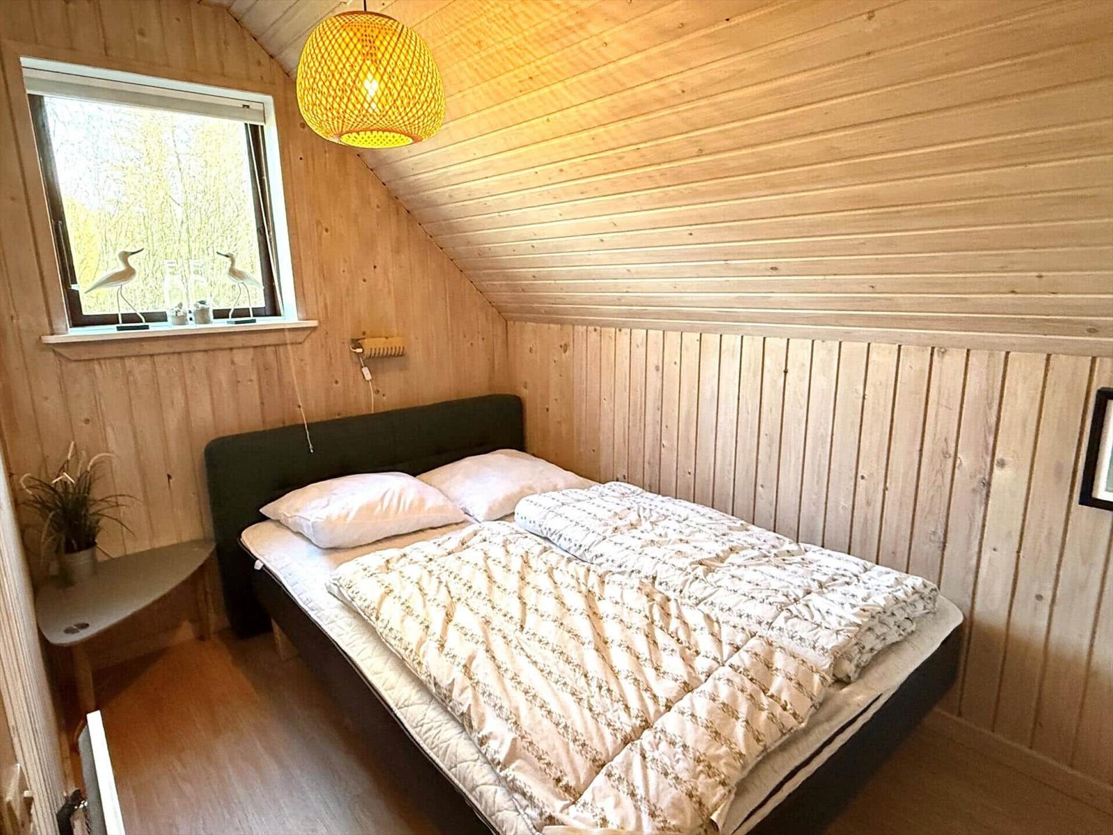 Schlafzimmer mit Holzwand, Bett und Fenster mit Vogeldekoration.