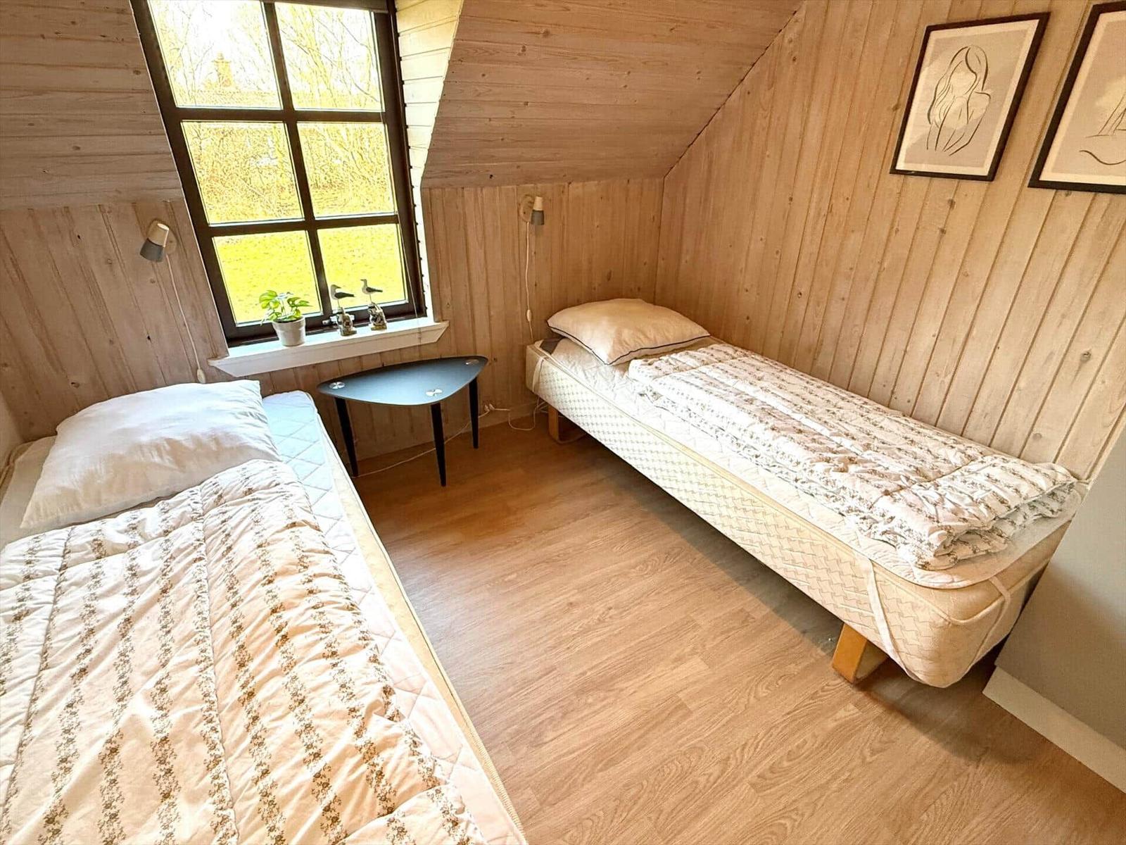 Zwei Betten in einem Holzraum mit Fenster und Tisch.