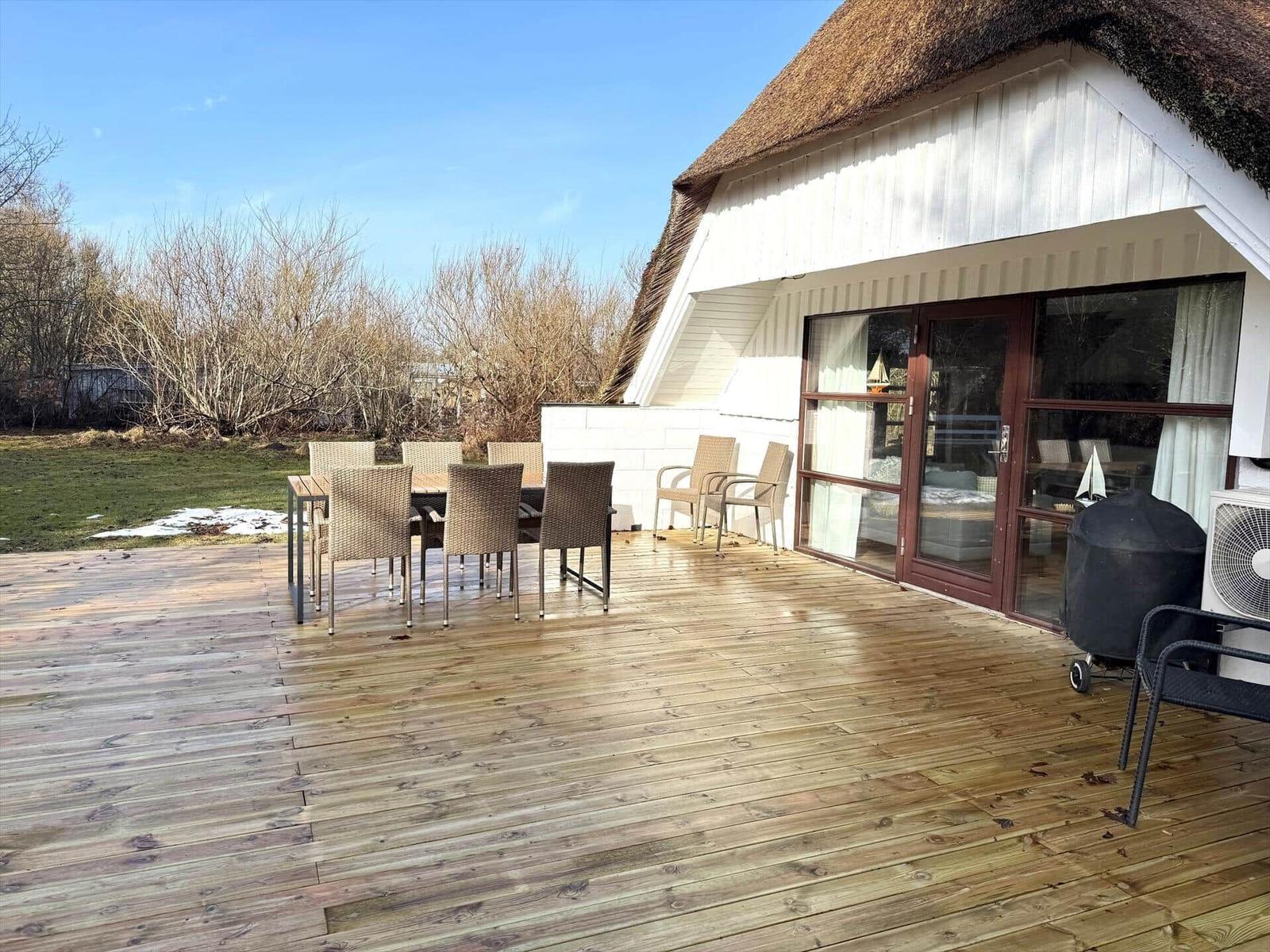 Terrasse mit Tisch und Stühlen, Grill und Glasfront zur Unterkunft.