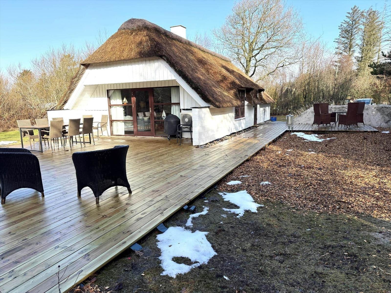 Haus mit Strohdach und Holzterrasse mit Gartenmöbeln und Reste Schnee.