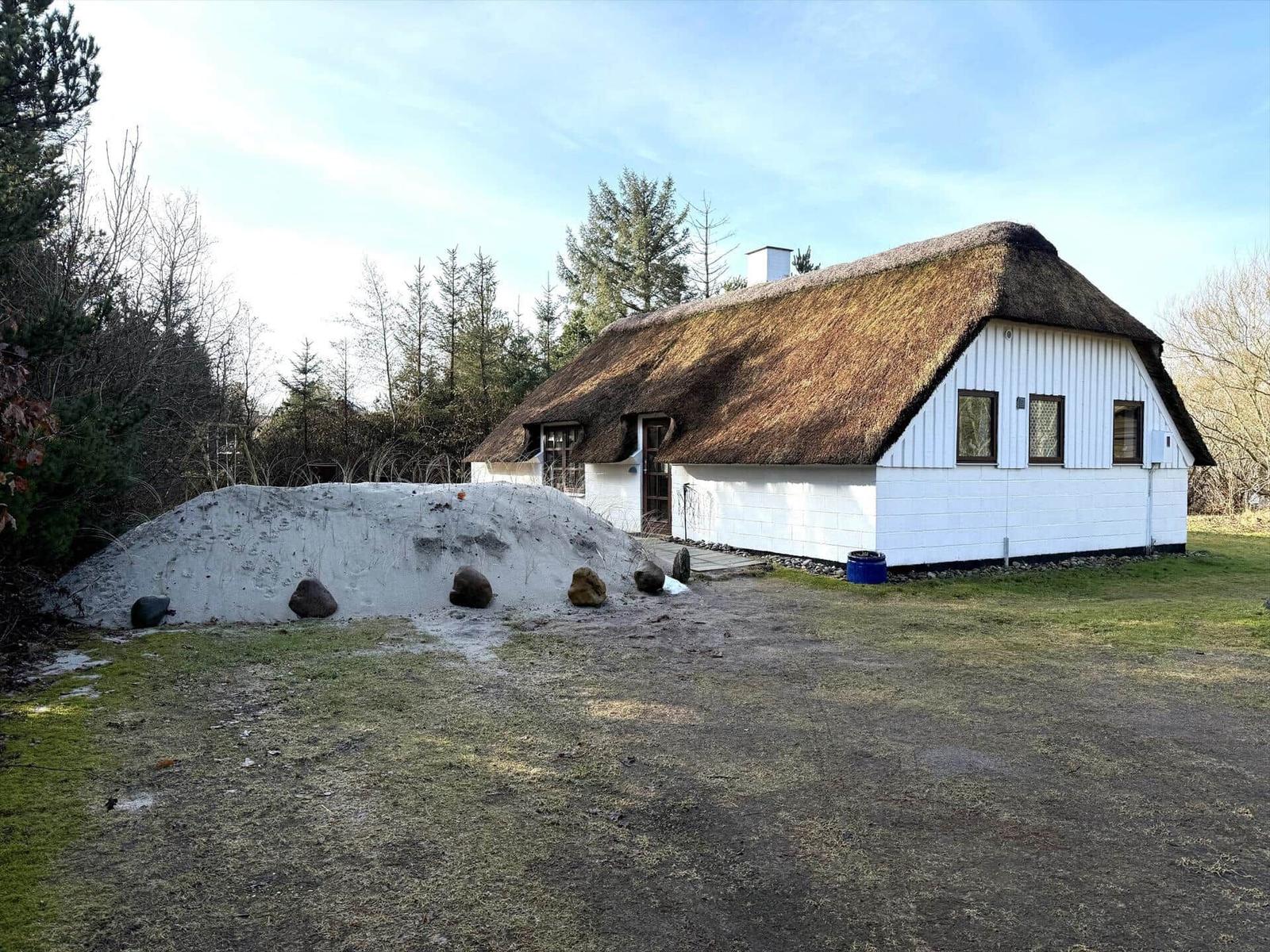 Haus mit strohgedecktem Dach und weißer Fassade, umgeben von Gras und Bäumen.