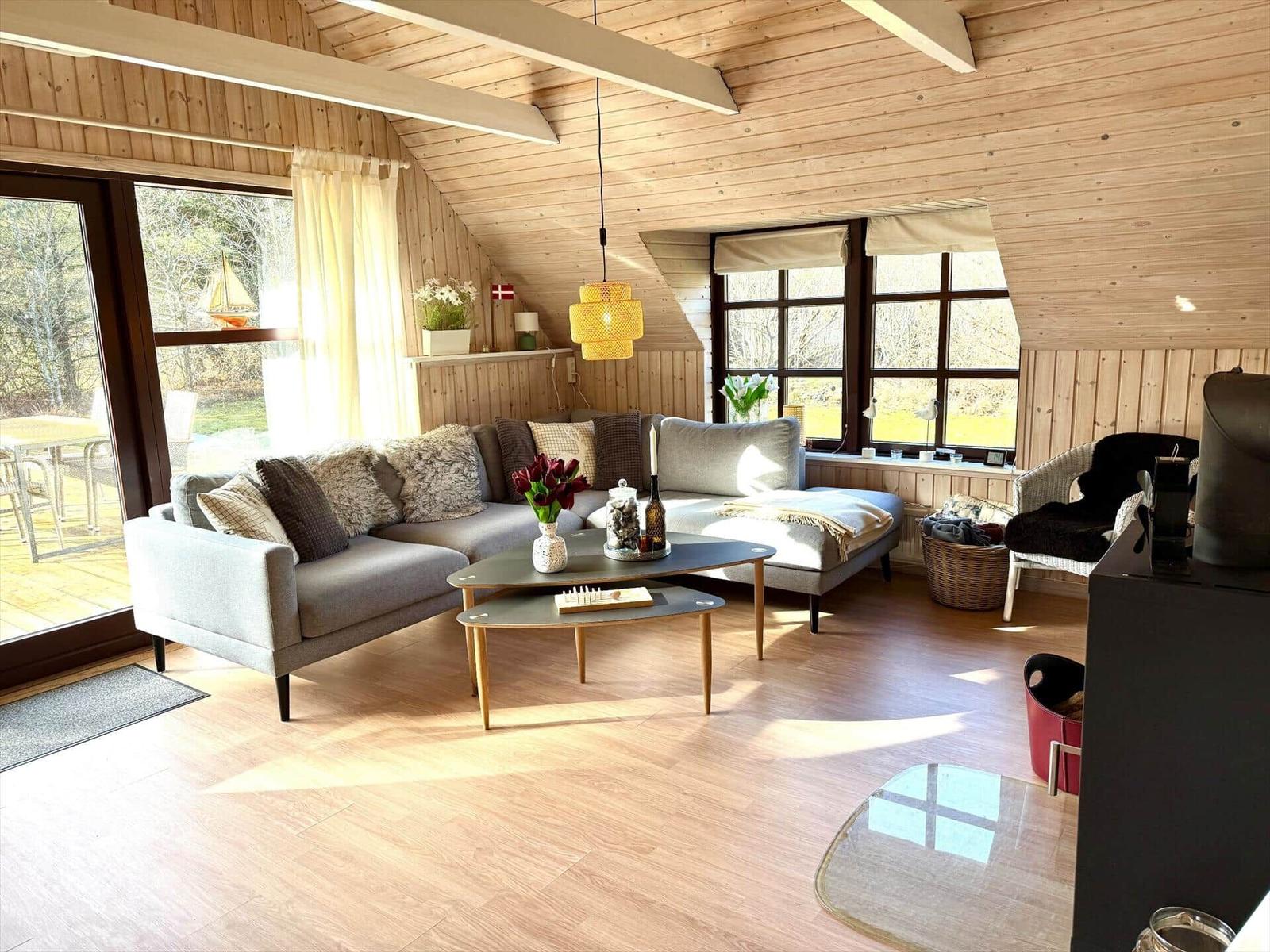Wohnraum mit Sofa, Tisch und Fenstern. Holzdecke und -wände.