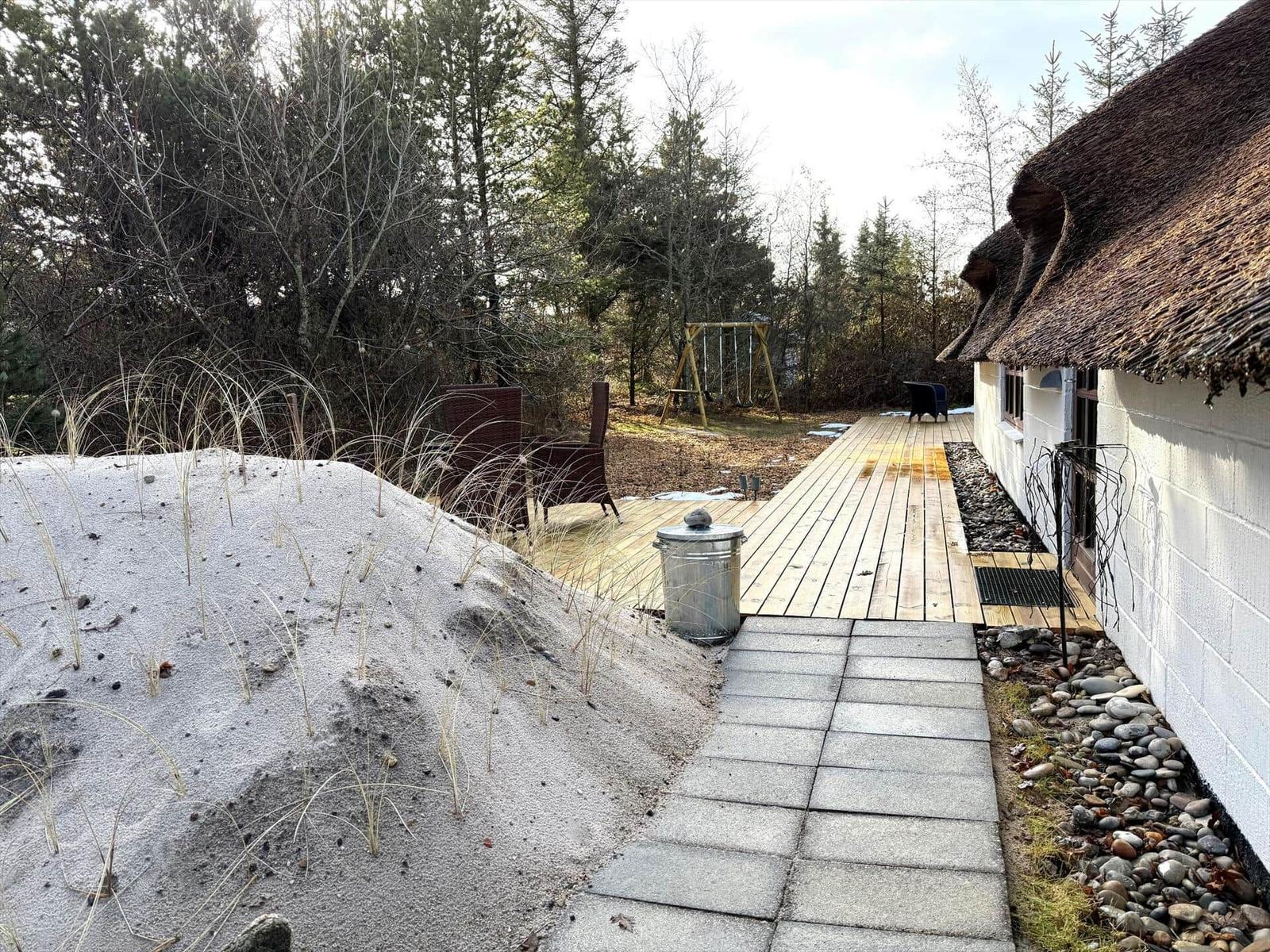 Haus mit Strohdach, Holzterrasse und Sandhügel im Wald