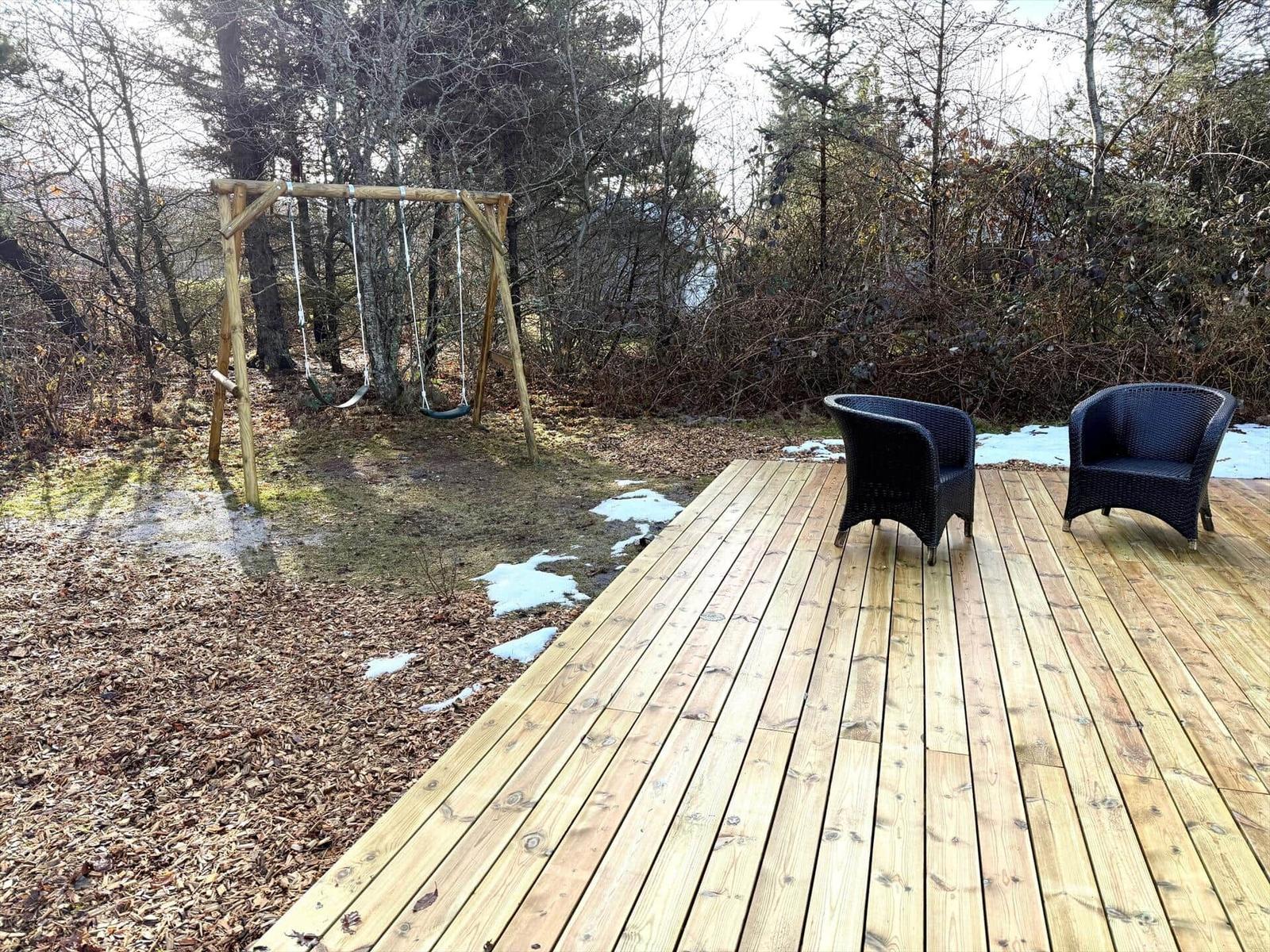Holzterrasse mit zwei schwarzen Sesseln und Schaukel im Wald.
