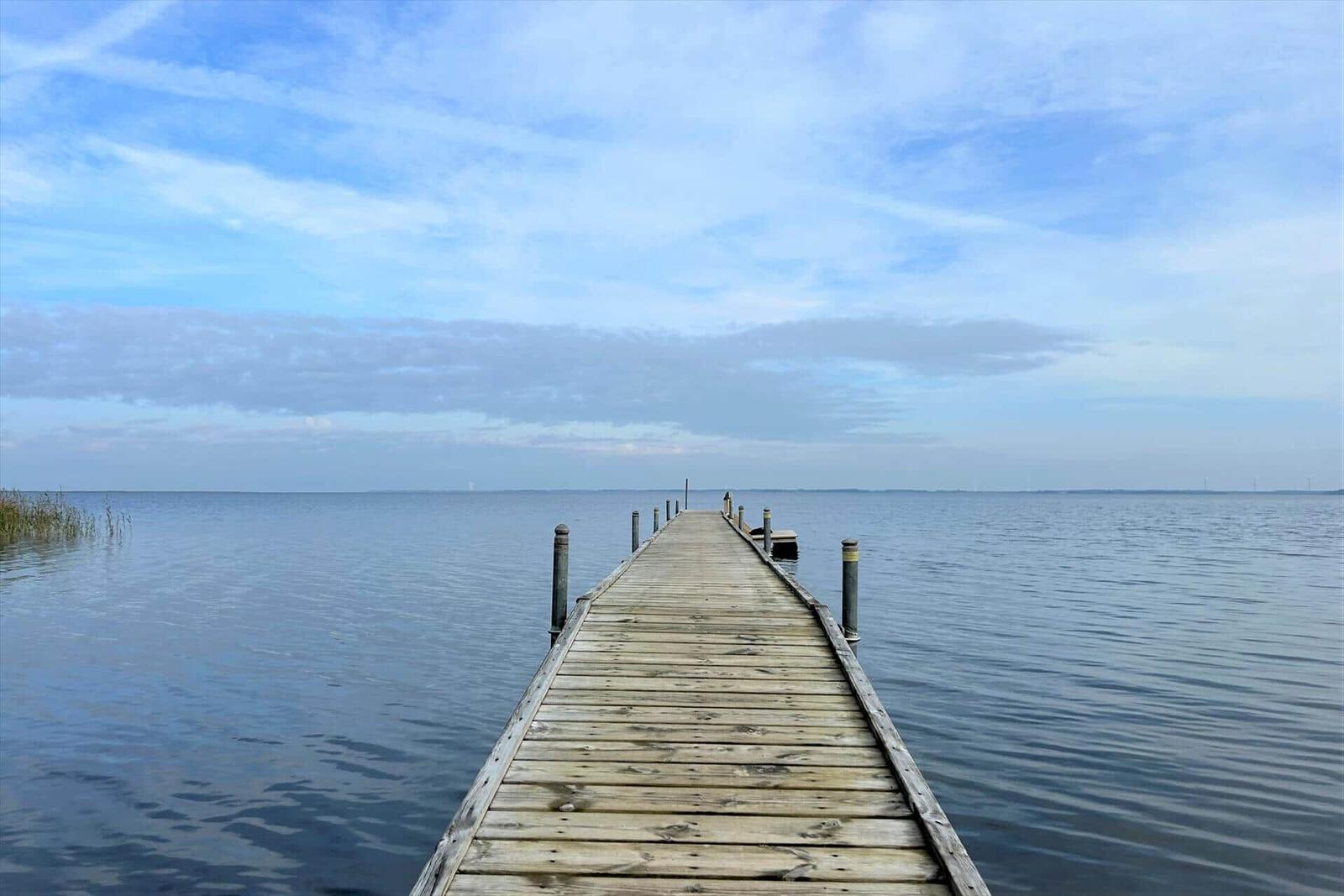 Holzsteg führt über ruhiges Wasser zu einem Boot.