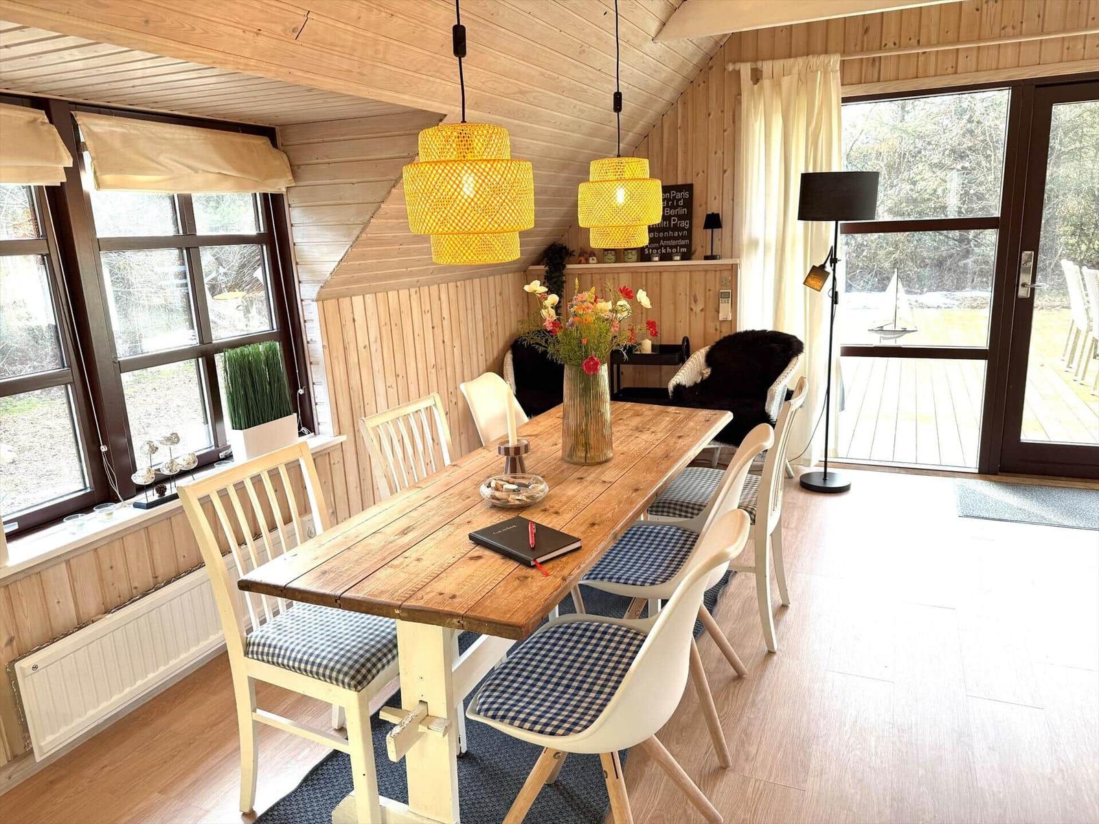 Esszimmer mit Holztisch, Stühlen und Fenstern. Hängelampen und Blick auf die Terrasse.