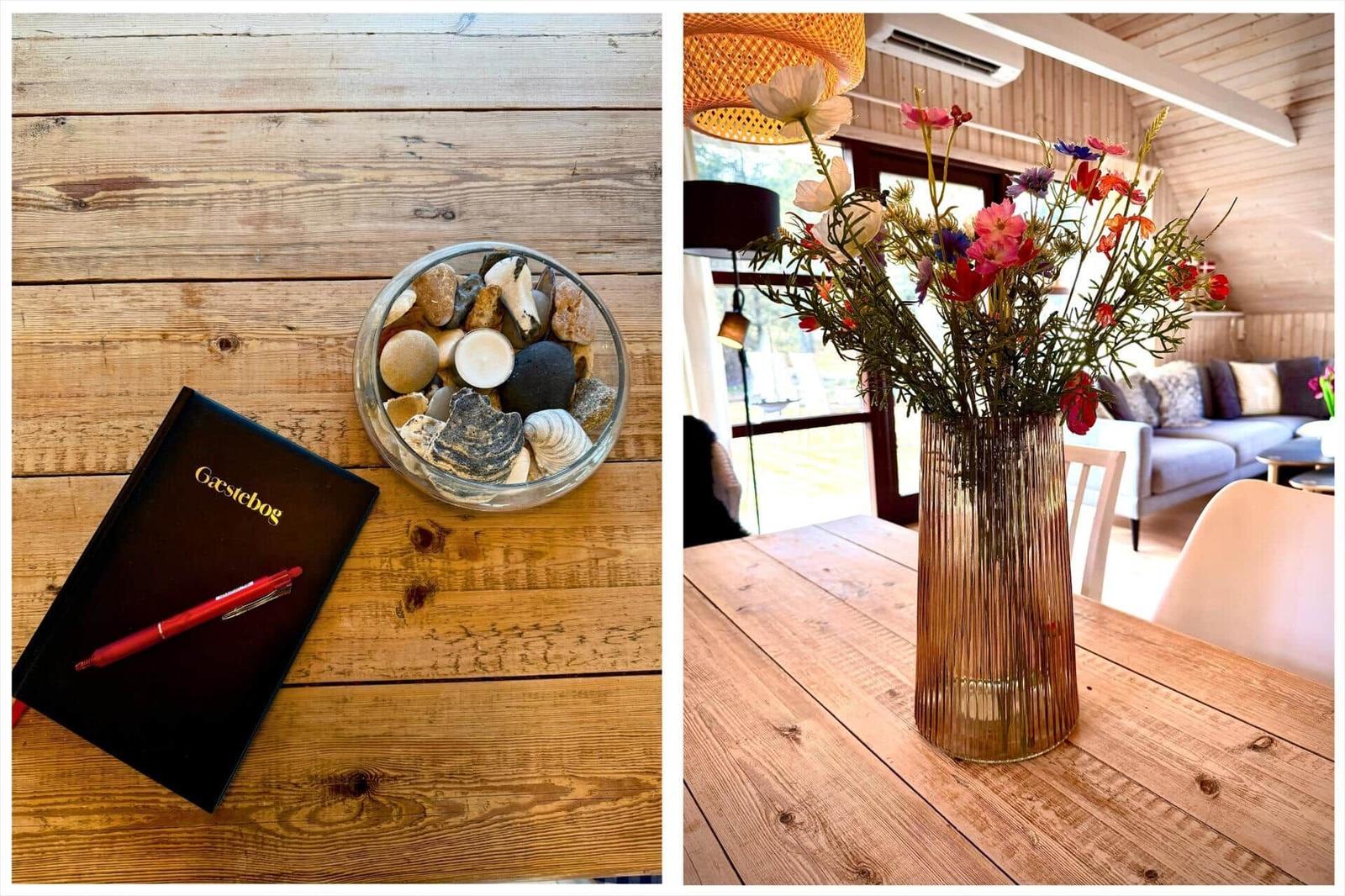 Gästebuch und Steinbecher auf Holztisch. Blumenarrangement auf Tisch mit Sofa im Hintergrund.