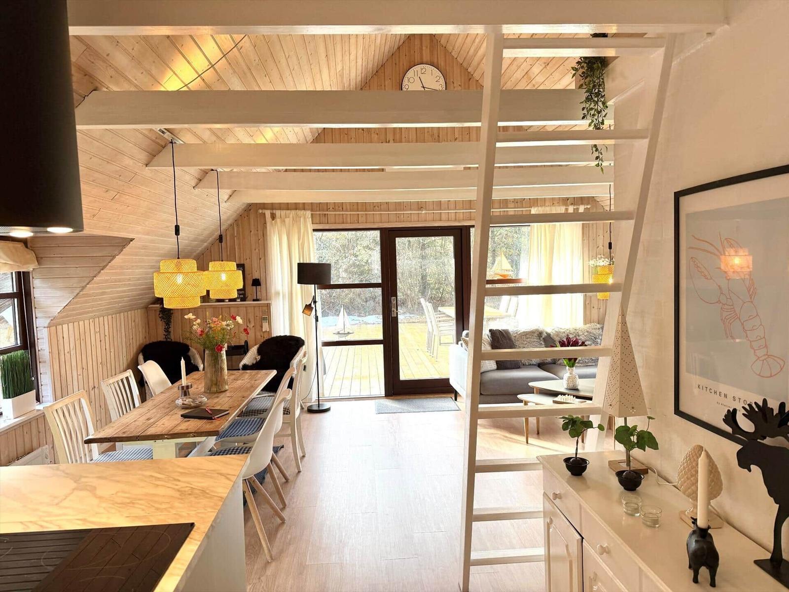 Haus mit Essbereich, Wohnbereich und Terrasse. Holzdecke, Treppe und Fenster sichtbar.