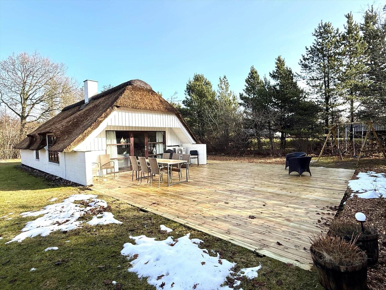 Haus mit Strohdach und großer Holterrasse mit Tisch und Stühlen.