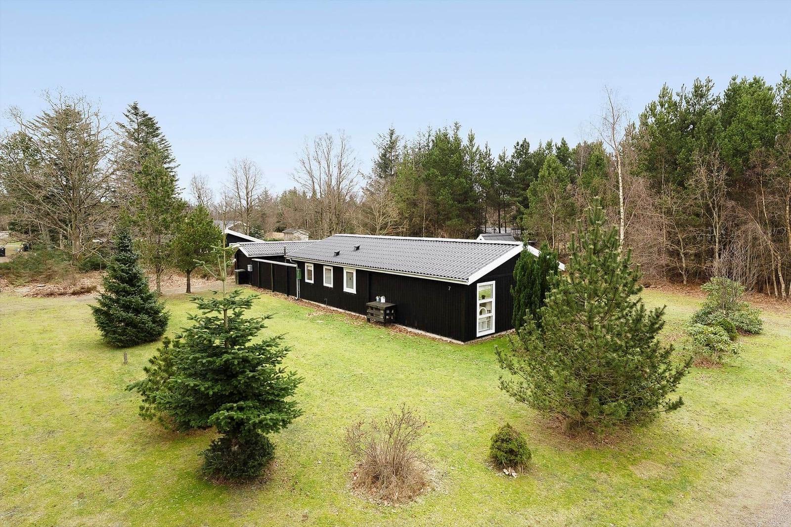 Black house with gray roof, surrounded by grass and trees.