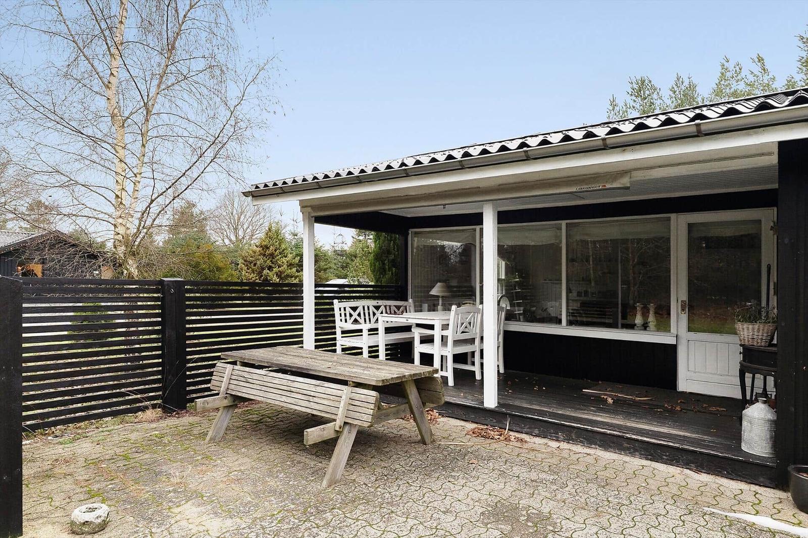 House with terrace, white table and chairs, wooden bench and black fence.
