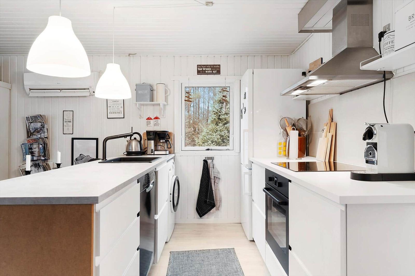 Kitchen with white cabinets, countertop, and window to the forest.