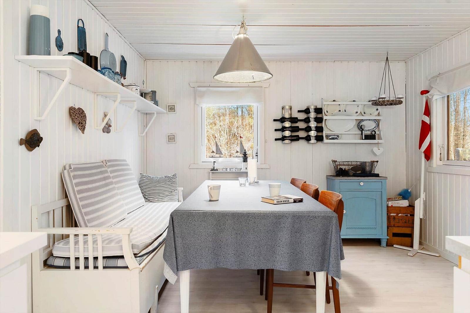 Dining room with table, chairs, and blue cabinet. Windows overlook the forest.