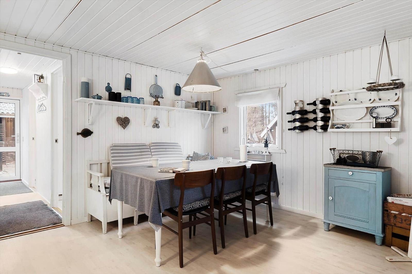 Dining area with table, chairs, and wall shelves. Wooden walls and ceiling. Window with view outside.