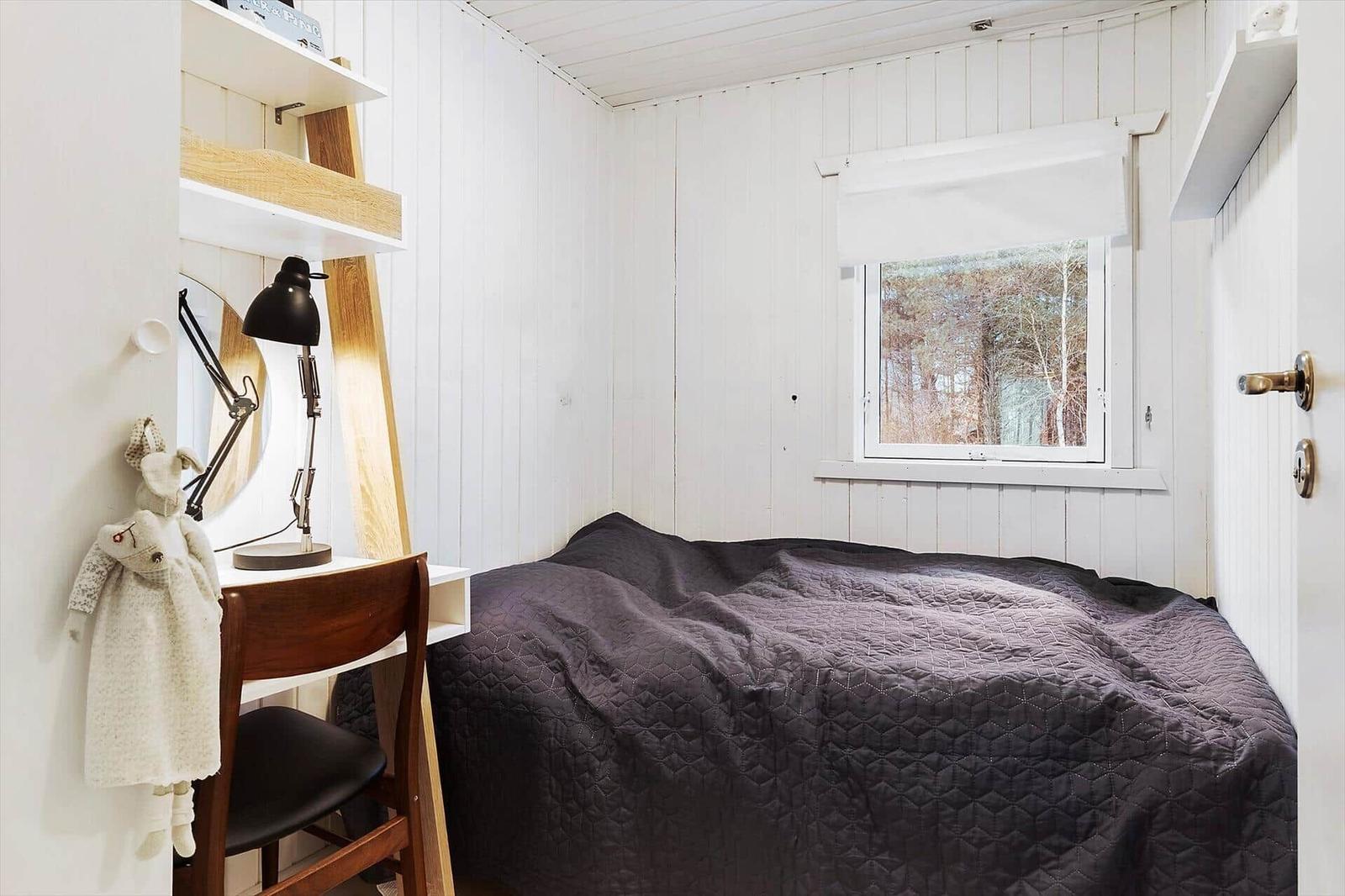 Bedroom with bed, desk, and window to the forest.