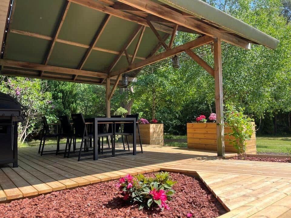 Holzterrasse mit Sitzgruppe, Grill und Pflanzenbeeten unter Dach