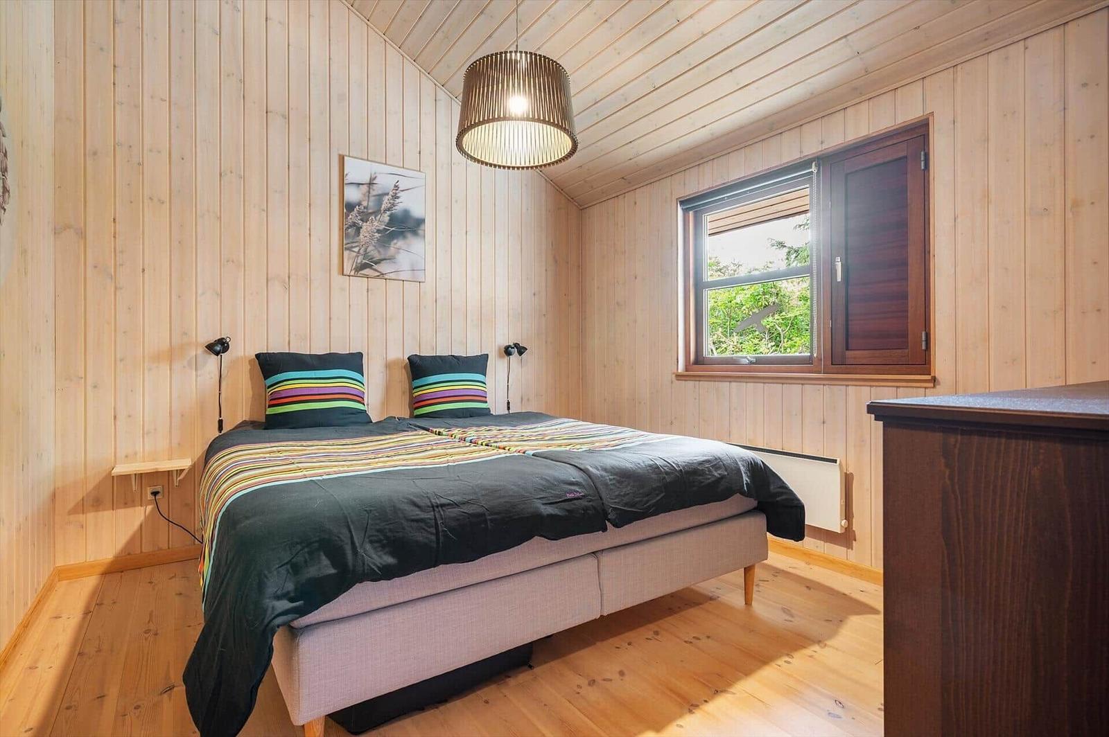 Schlafzimmer mit Holzwand, Bett und Fenster