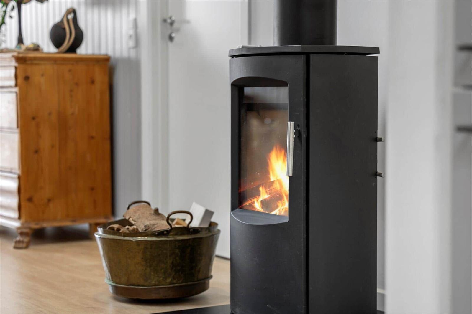 Holzofen mit brennendem Feuer und Kiste mit Brennholz im Raum.