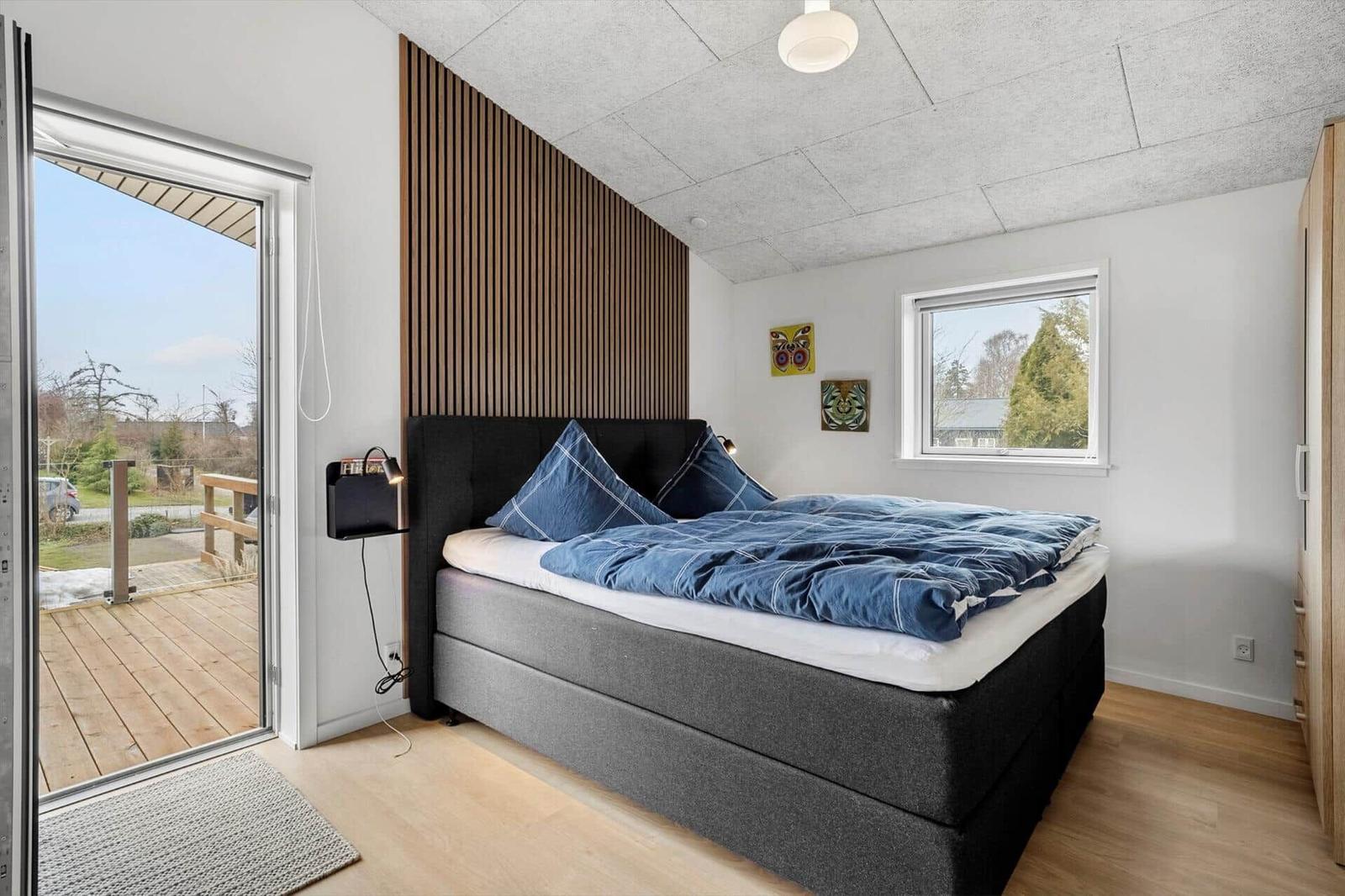 Schlafzimmer mit Bett, Fenster und Balkontür. Holzdecke und Wandverkleidung.