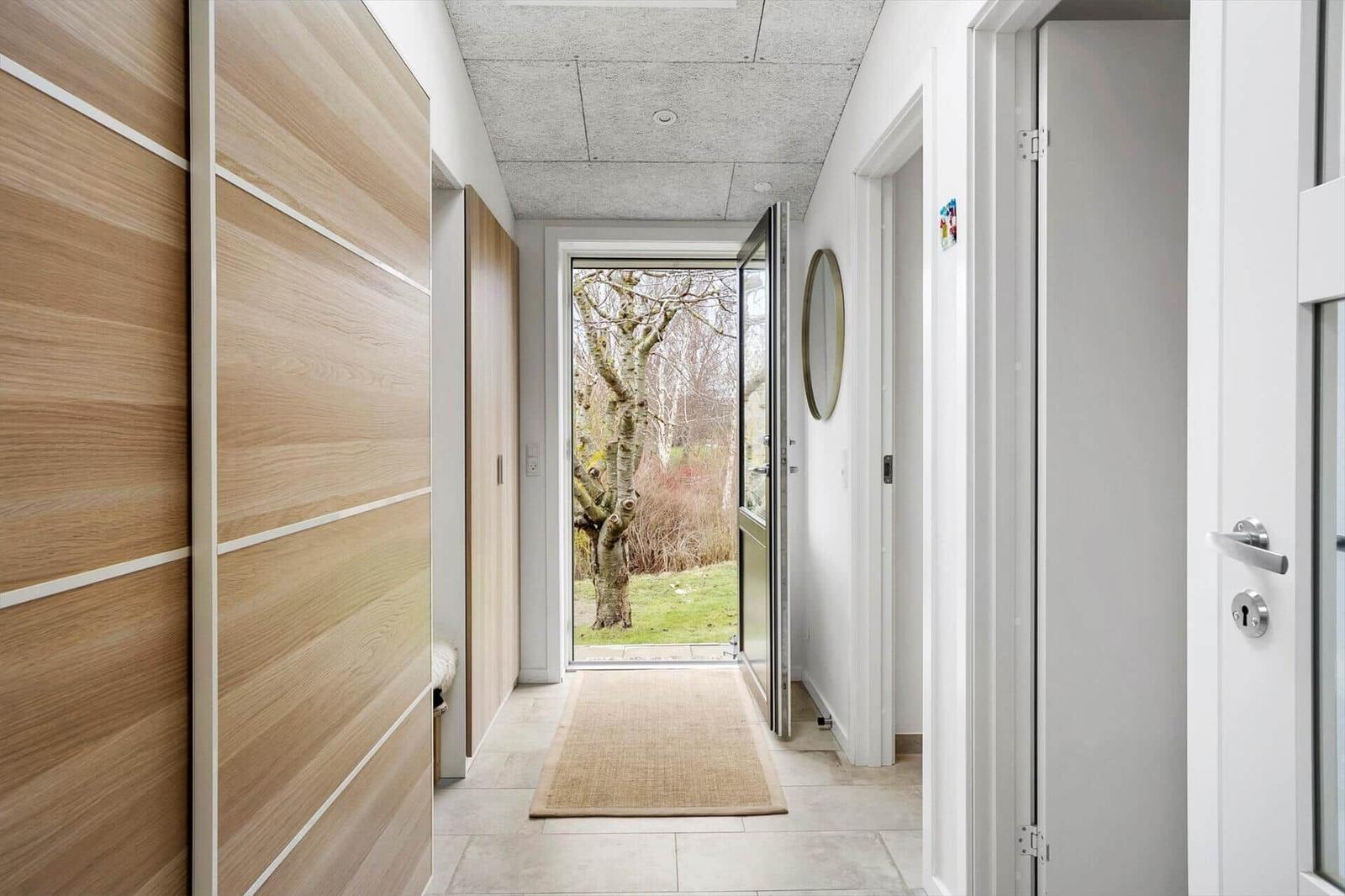Hallenflur mit Holzschrank, Tür zum Garten und runder Wandspiegel.