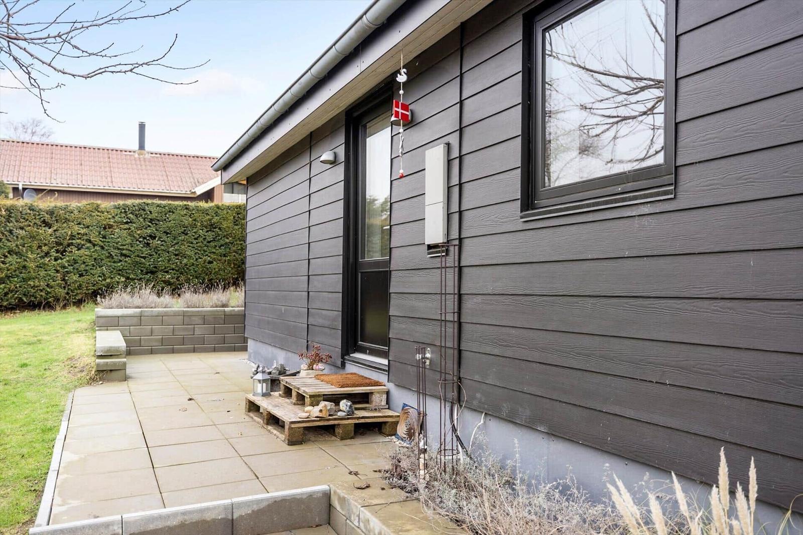 Haus mit grauer Fassade, Terrasse und Garten. Daneben hängt eine dänische Flagge.
