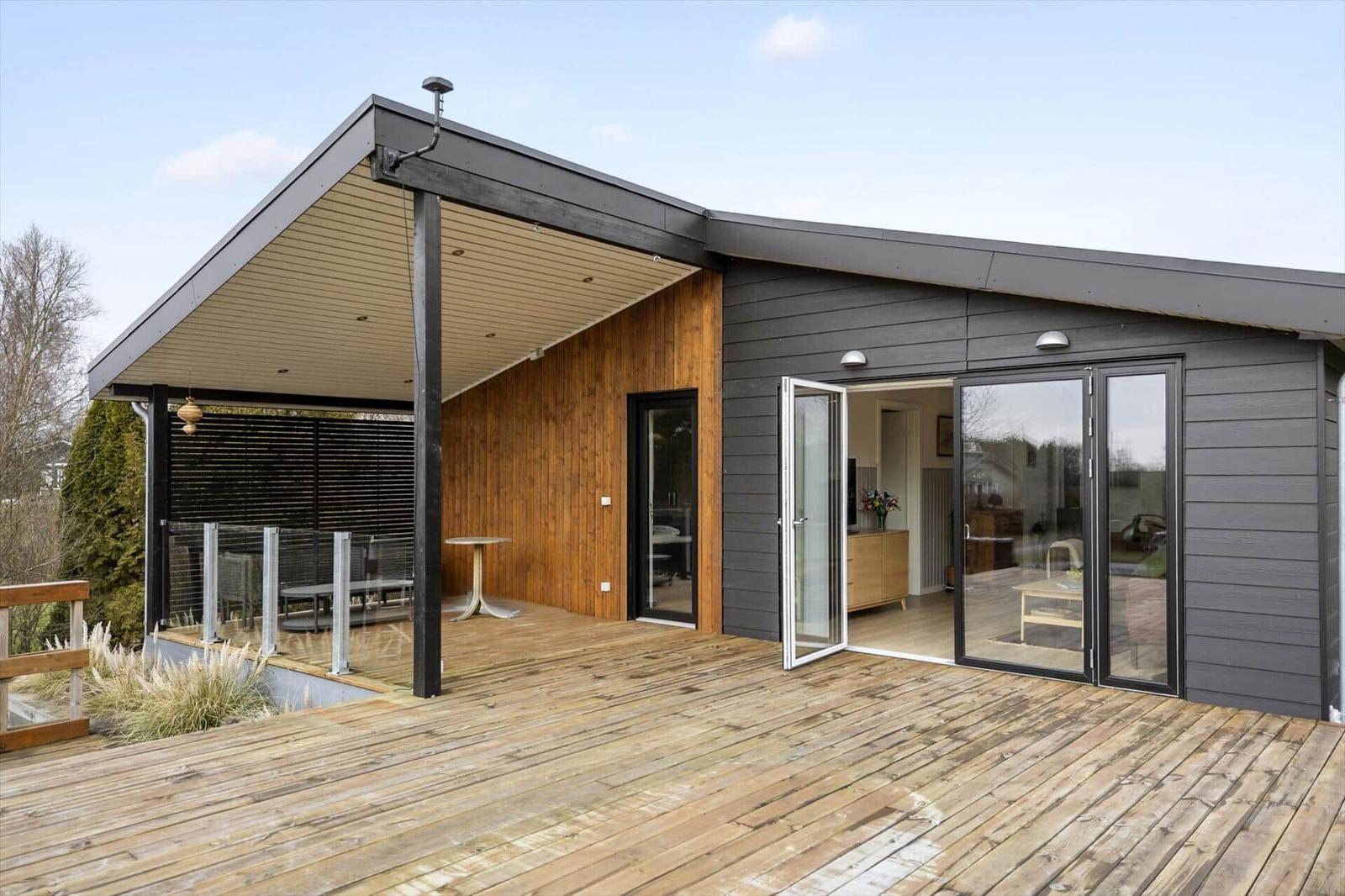 Moderne Villa mit Holzterrasse und Glasfronten. Terrasse mit Tisch und Sitzgelegenheit.