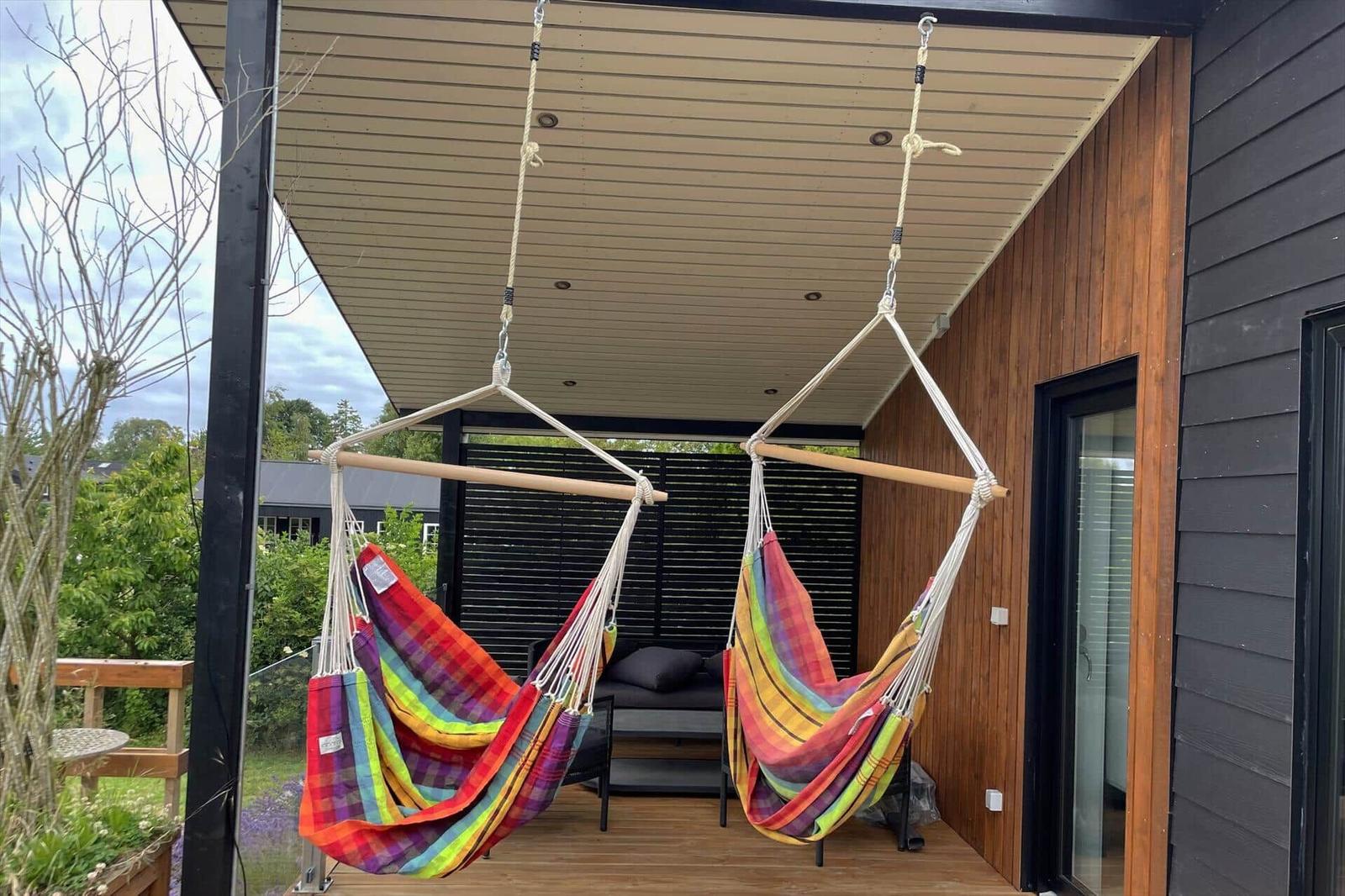 Zwei bunte Hängematten hängen unter einem Dach auf einer Terrasse.