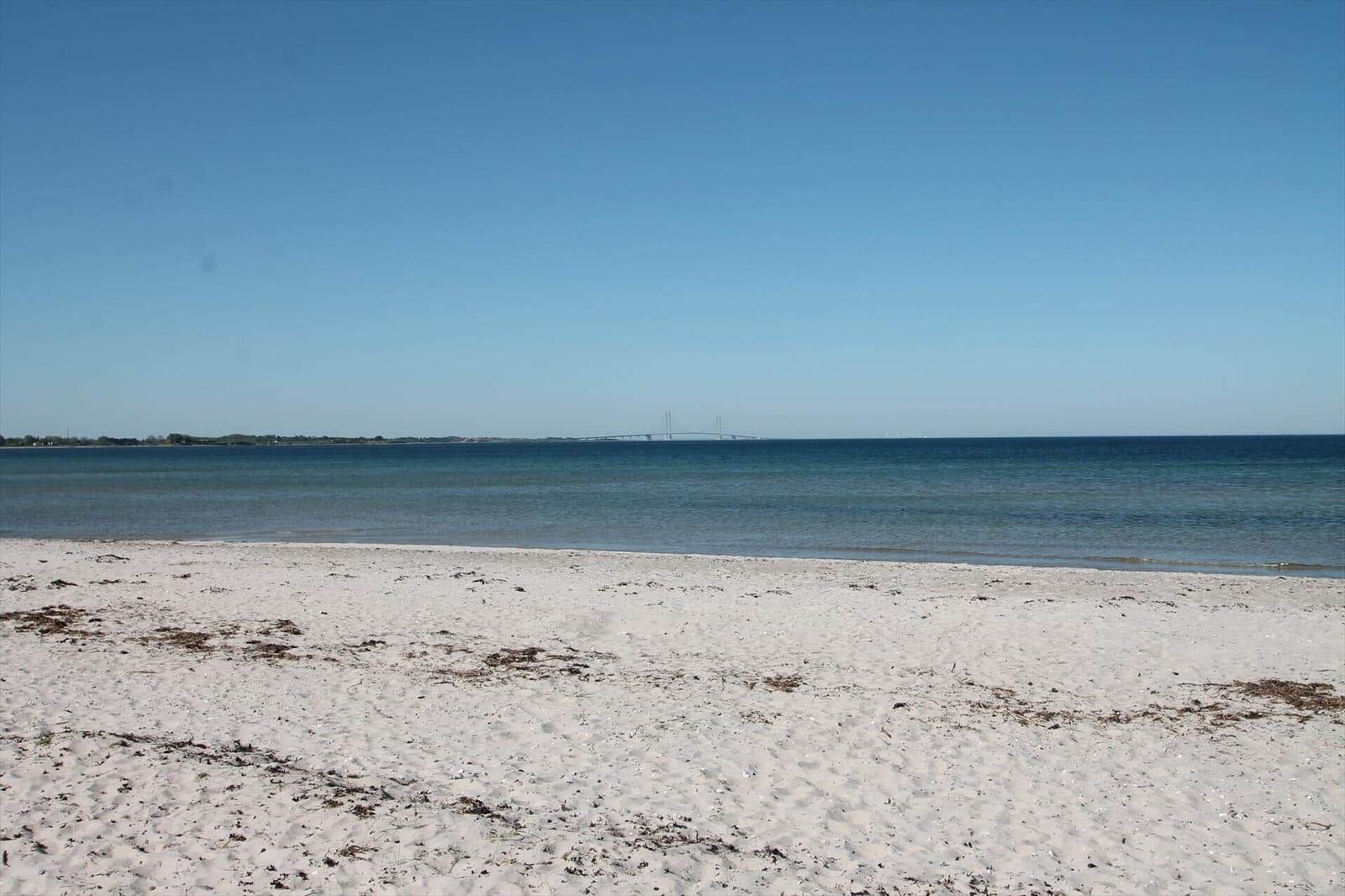 Weißer Sandstrand mit Blick auf Meer und Brücke im Hintergrund.