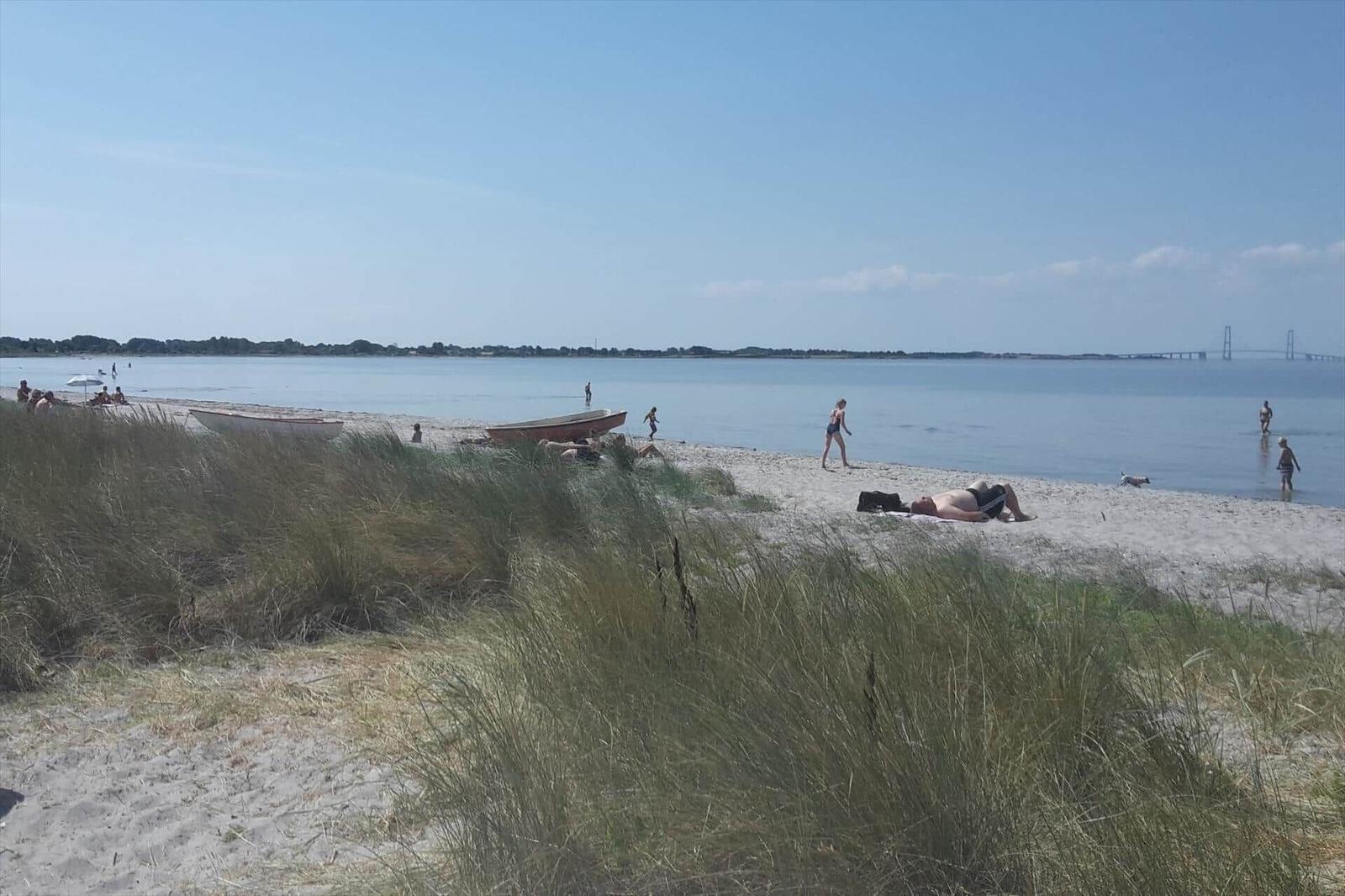 Strand mit Watt, Dünen und Booten. Menschen baden und sonnen.